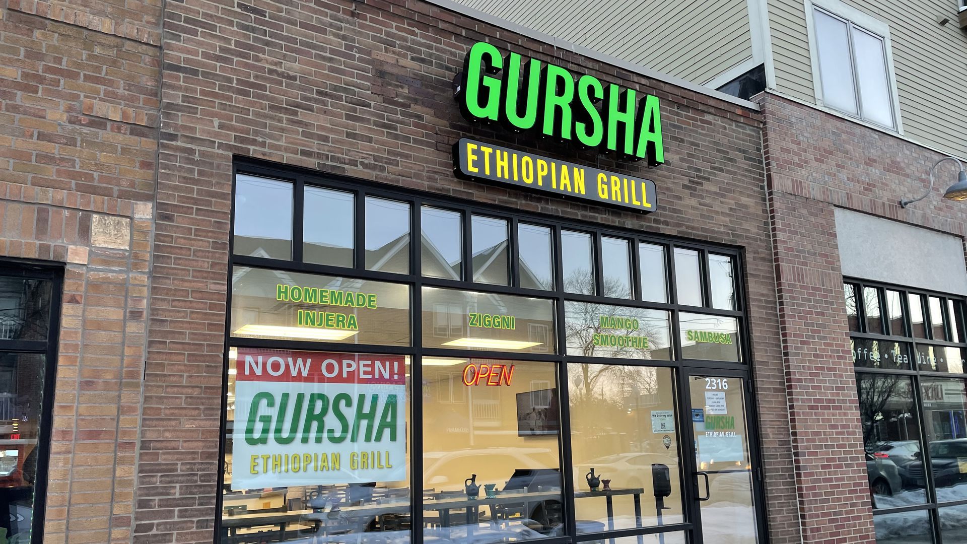 Picture of the outside of Gursha Ethiopian Grill, it's a brown brick building with glass windows and a big green sign that spells out the name.