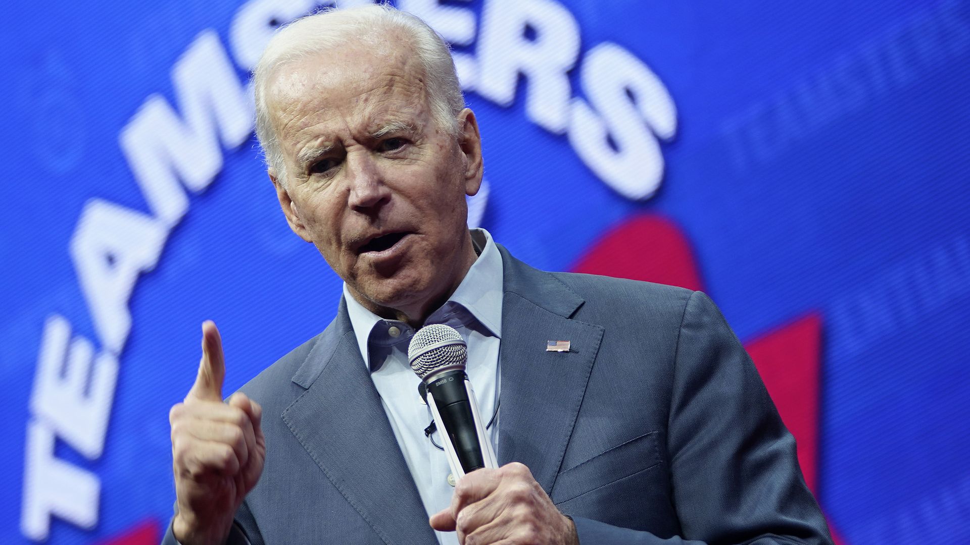 Joe Biden talks into a microphone with a finger raised.