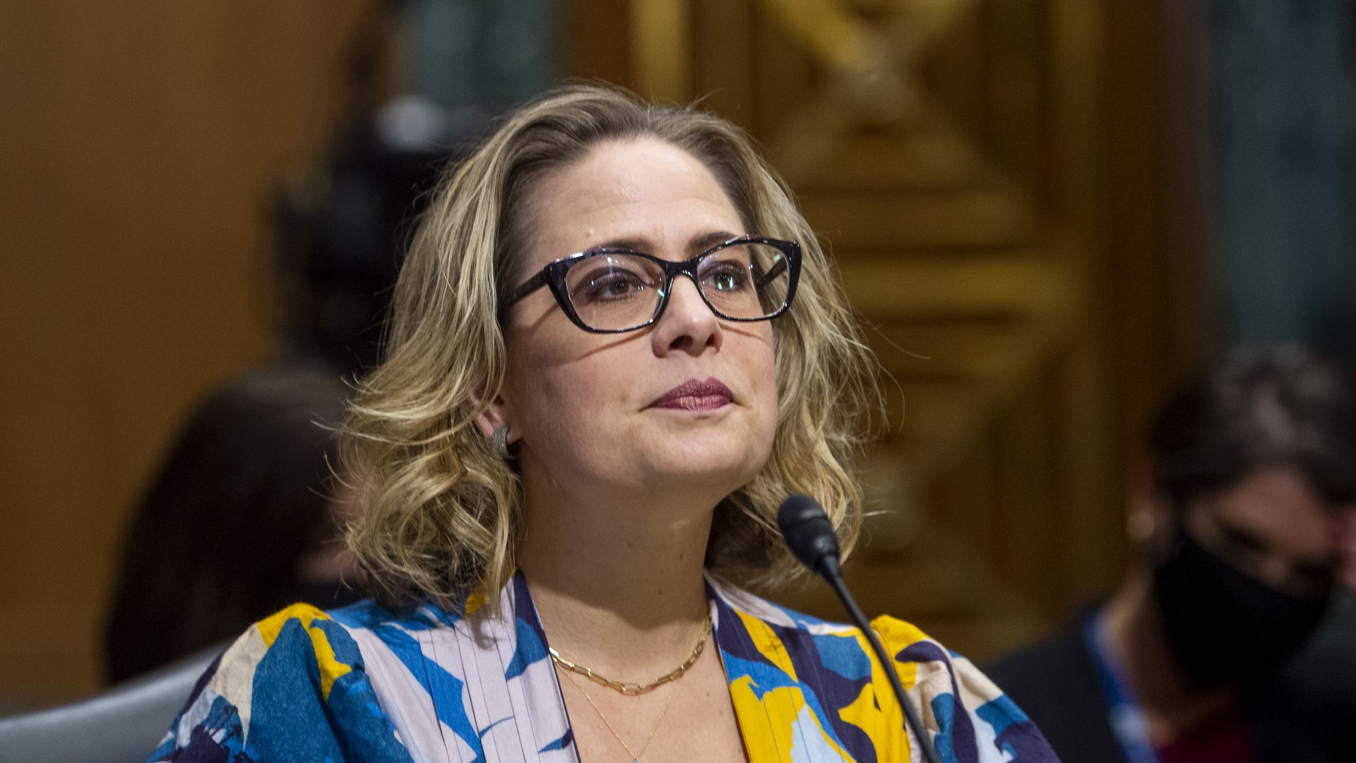 Photo of Kyrsten Sinema sitting in front of a mic with pursed lips