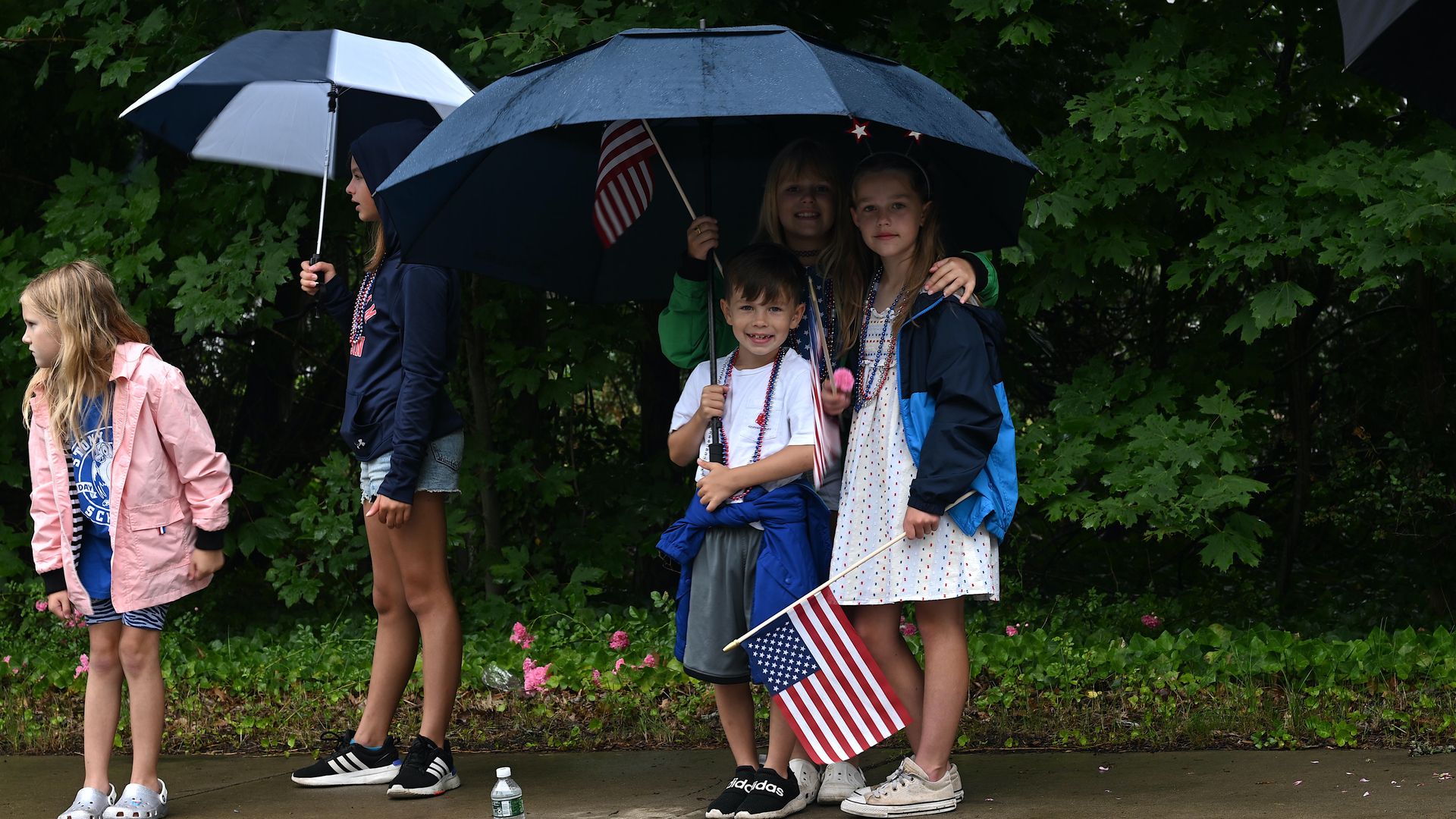 Children huddle under umbrellas during a rainstorm on July 4, 2023.