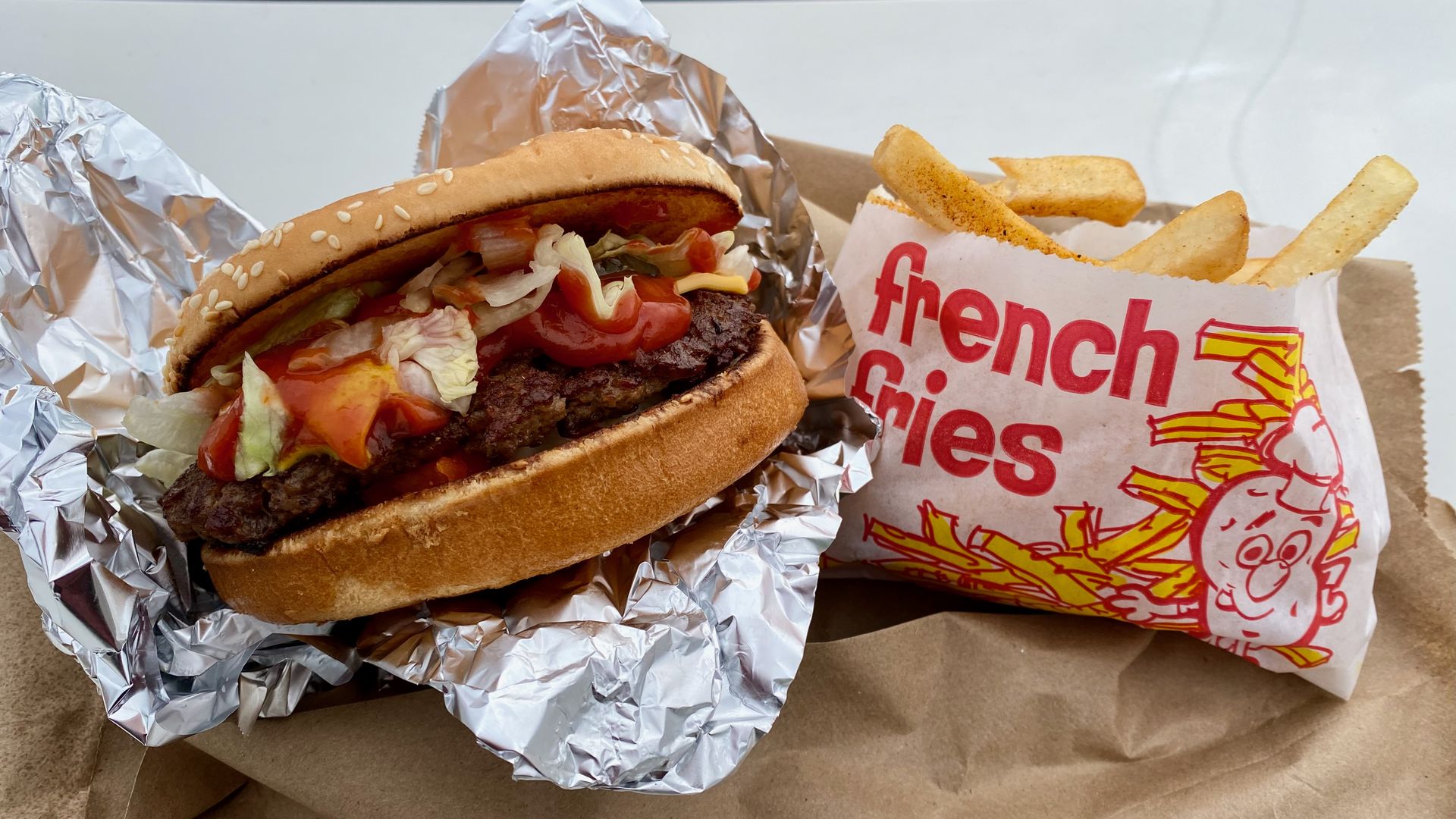 A burger in foil next to a bag of fries that reads "french fries"