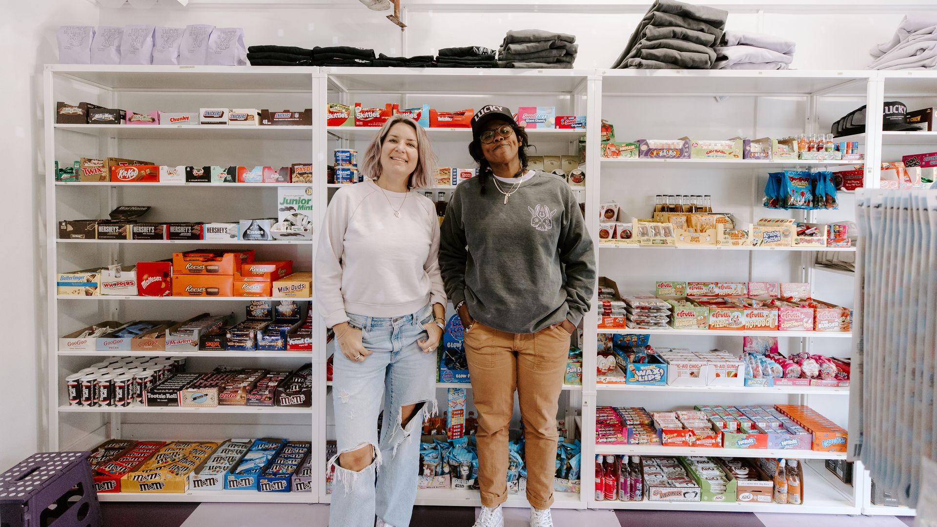 Two women standing in front of a wall of candy.