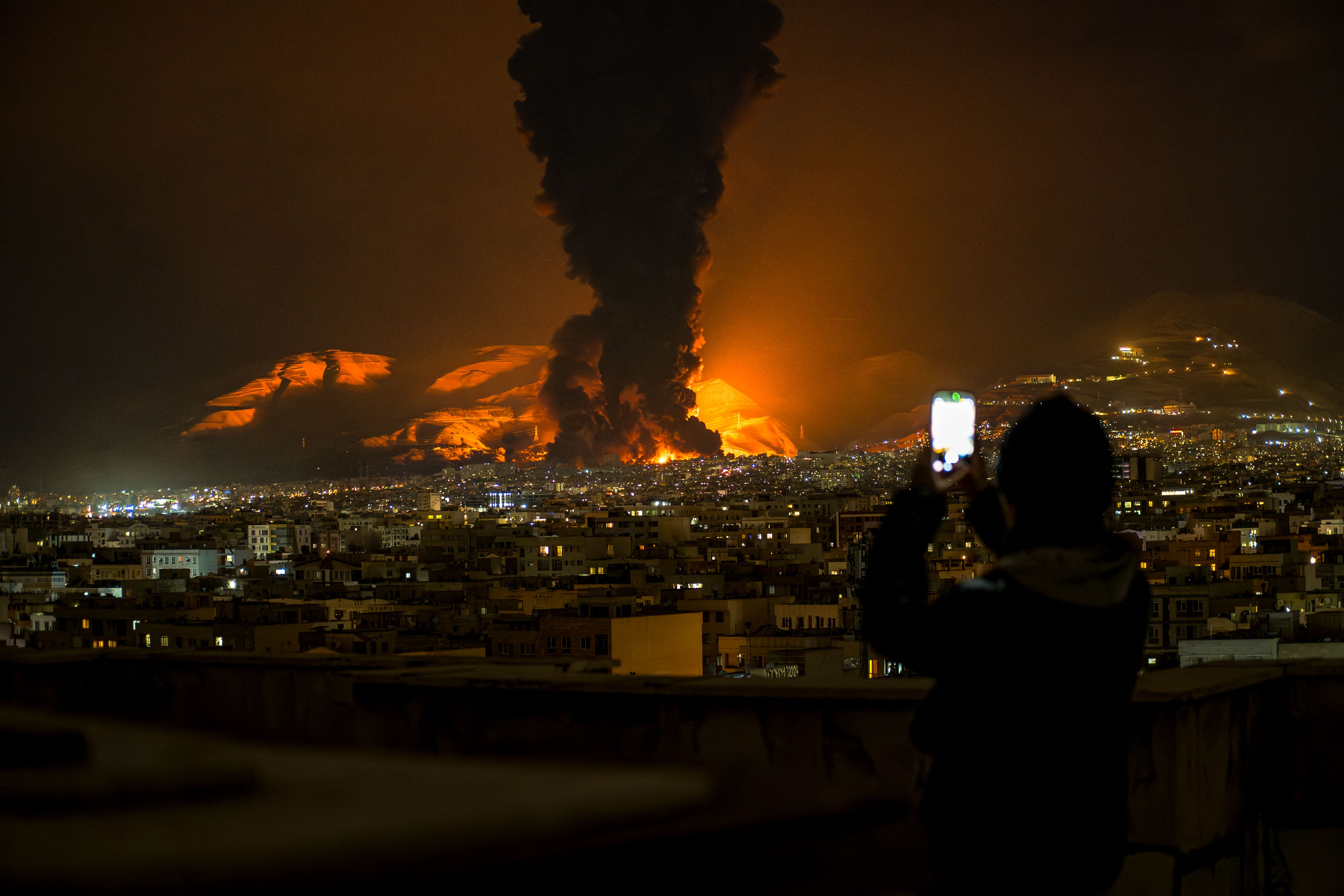 A woman takes a video of smoke rising from a Tehran oil depot after an Israeli strike on Saturday.