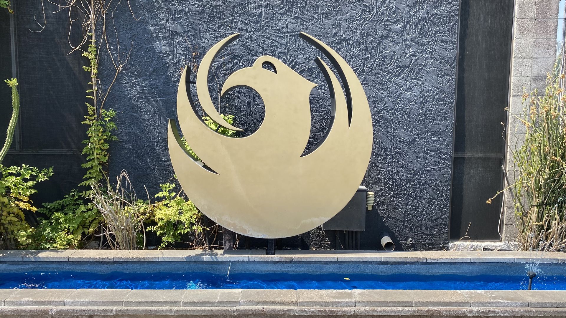 A circular bird emblem in front of a long thin water feature. 