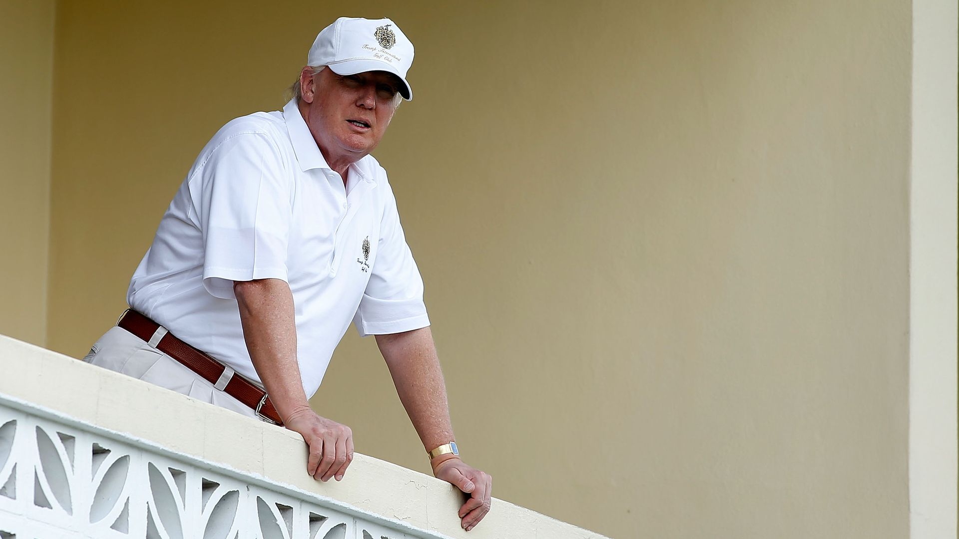 In this image, Trump stands in a white polo shirt and khakis and leans on a white balcony.