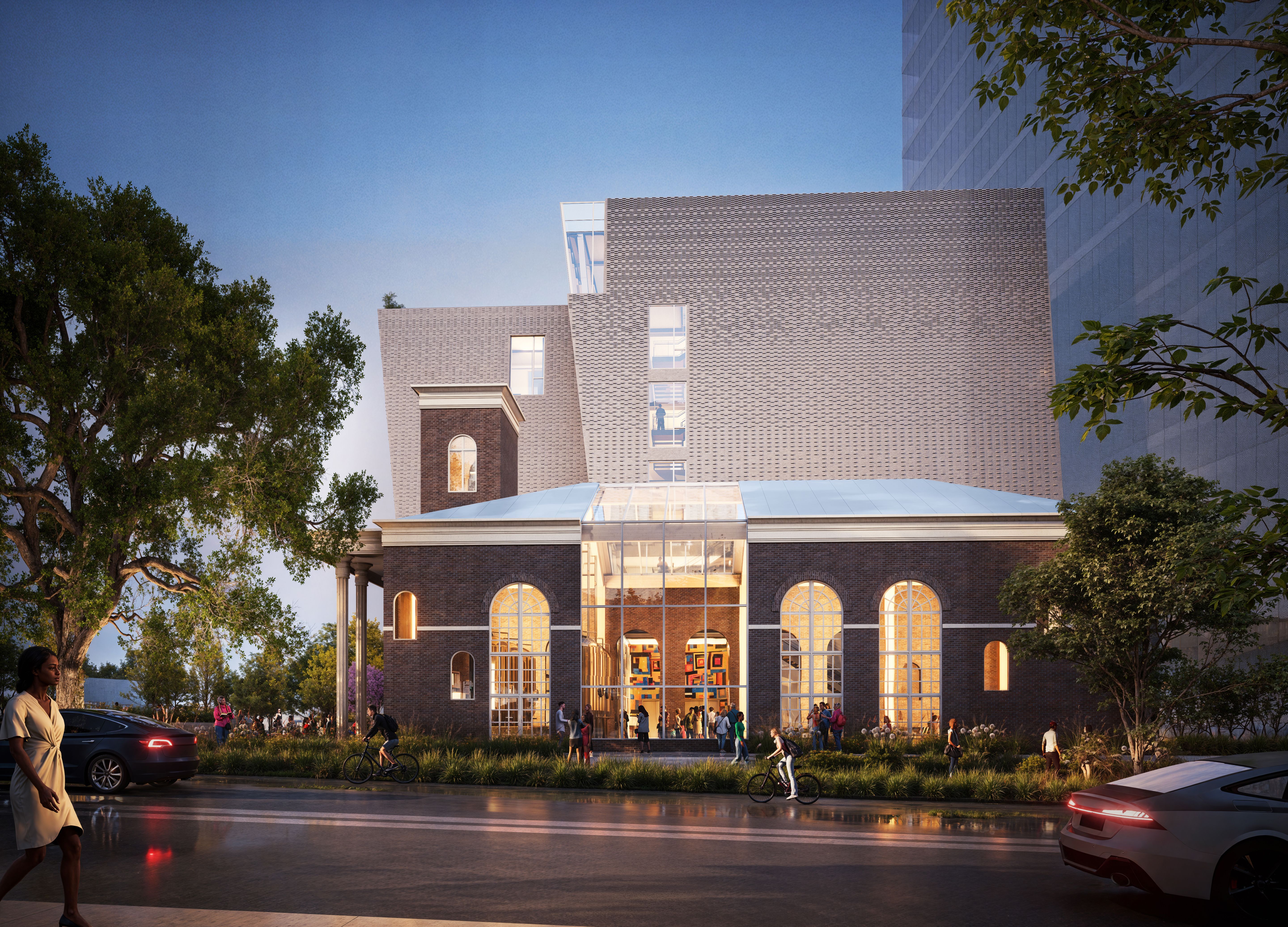 Evening scene of a large brick building with arched windows and a glass entrance, people walking and biking nearby, surrounded by green trees and modern structures.