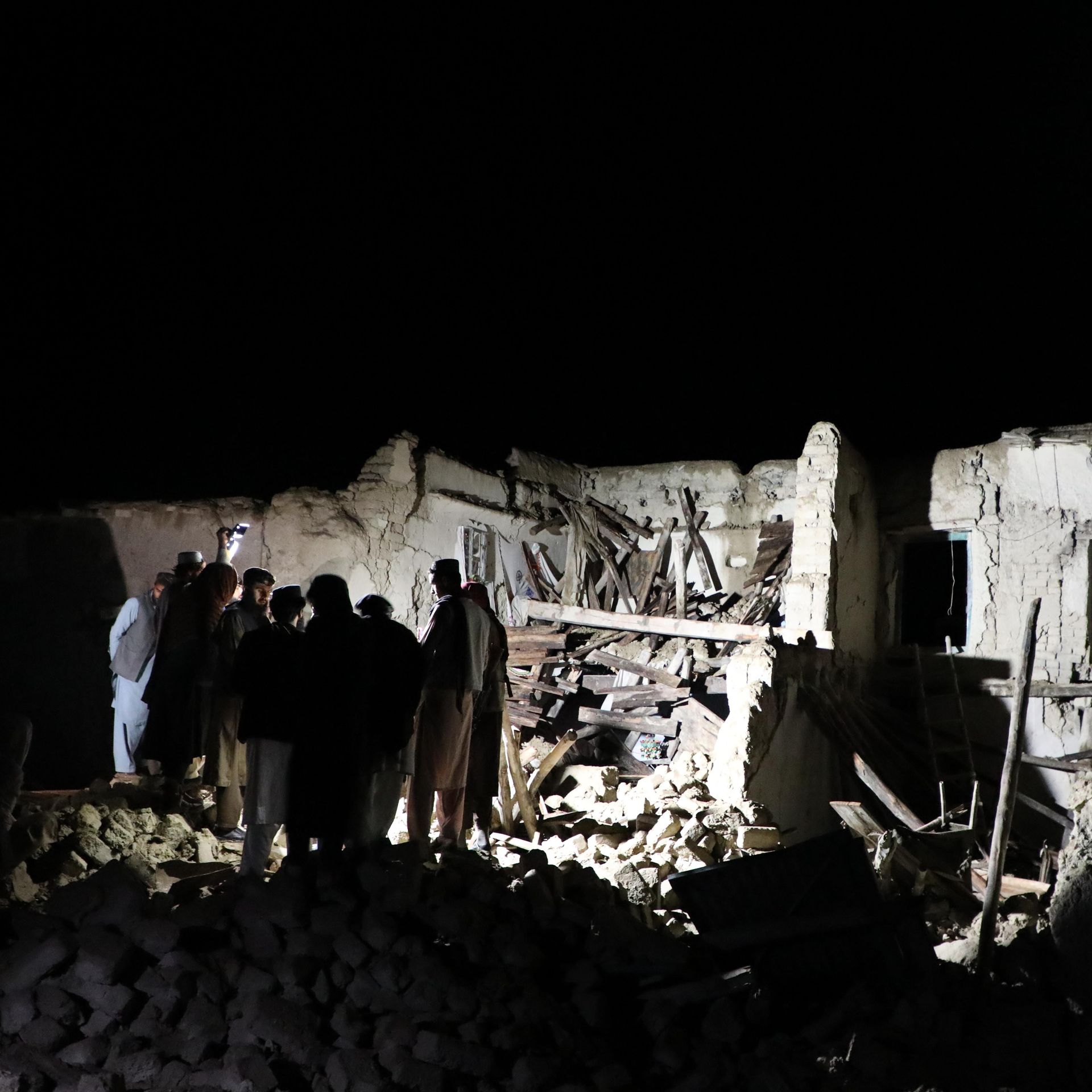 A group of people searching through rubble in the dark. 
