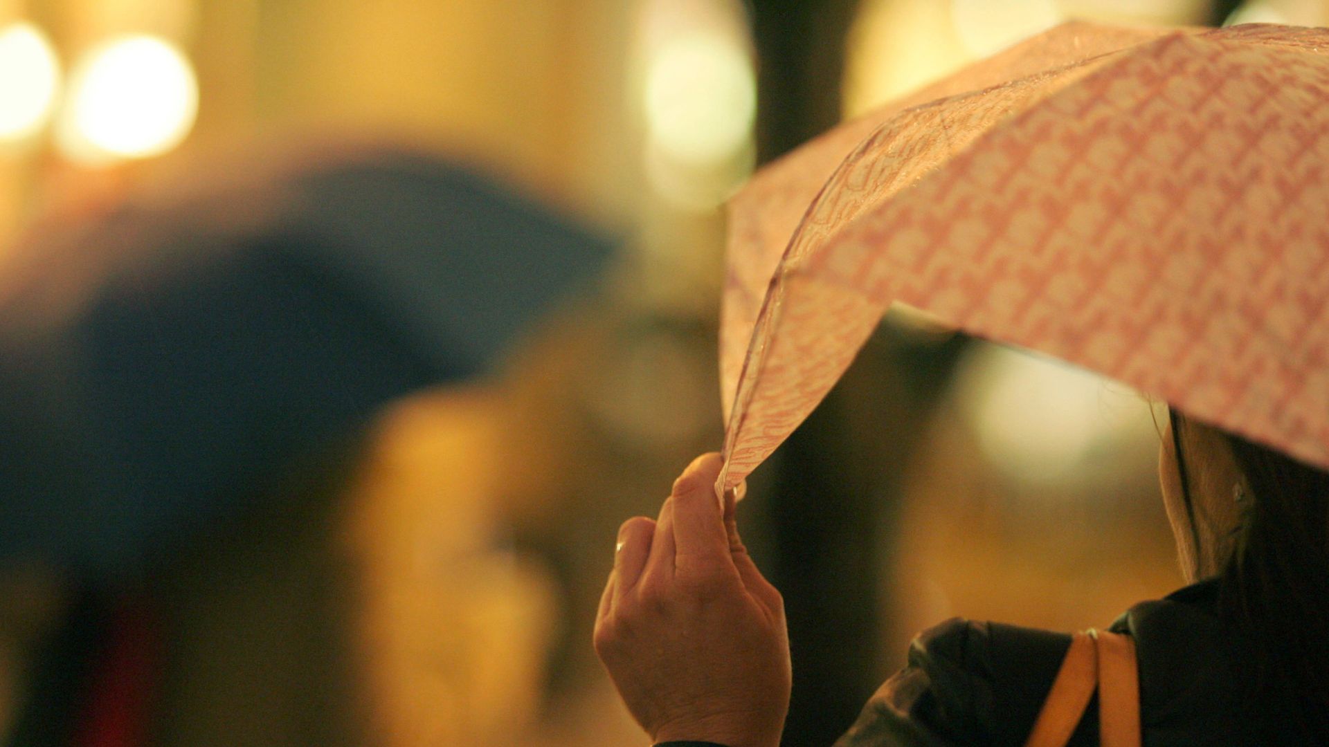 A person holds the edge of an orange-tinged umbrella. A blurry view of a city street is in the background.