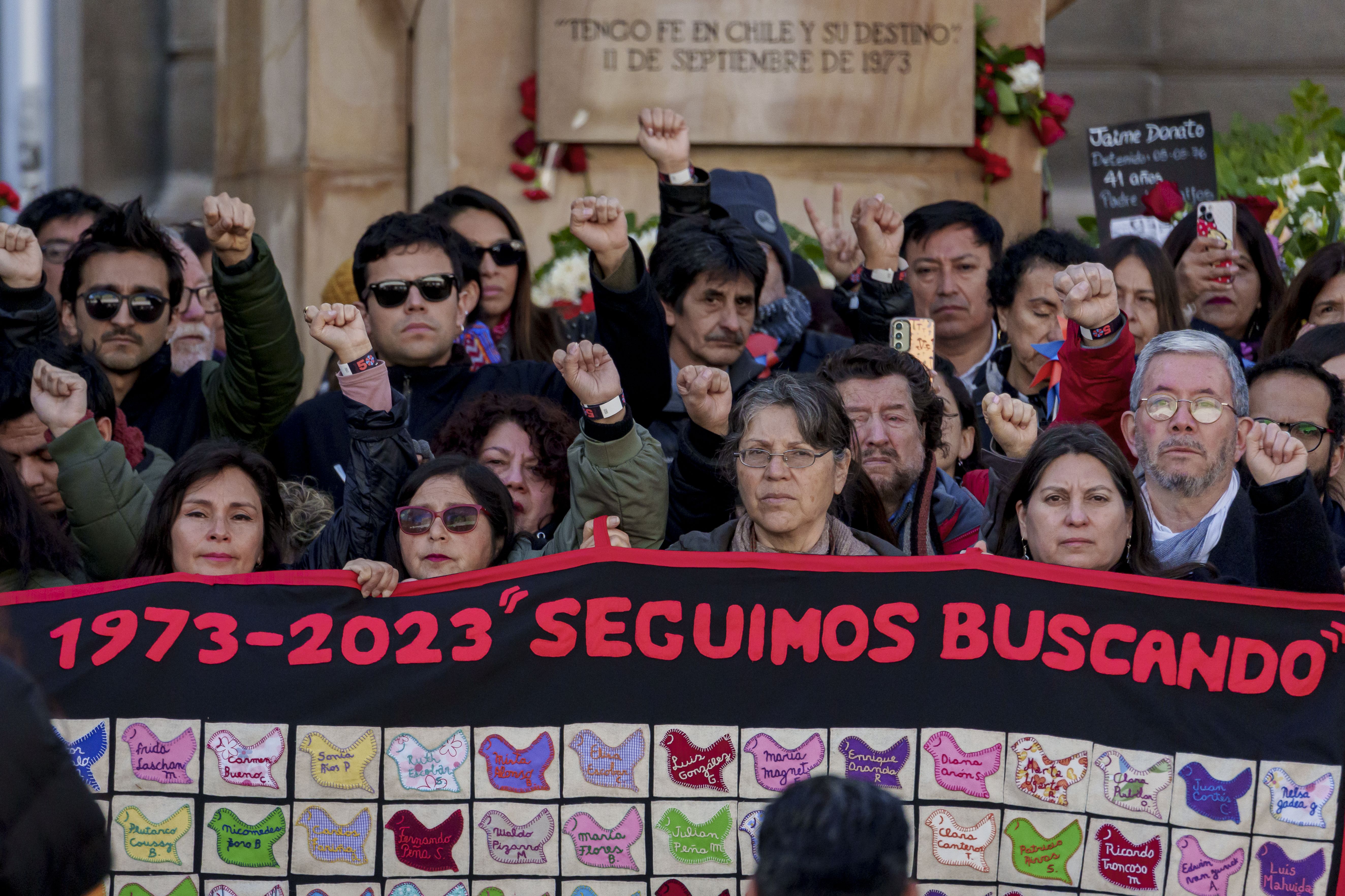 Many people hold their fists in the air while marching in Chile to commemorate the 50-year mark of the coup that overthrew the government. They hold a banner saying "1973-2023: We're still searching"