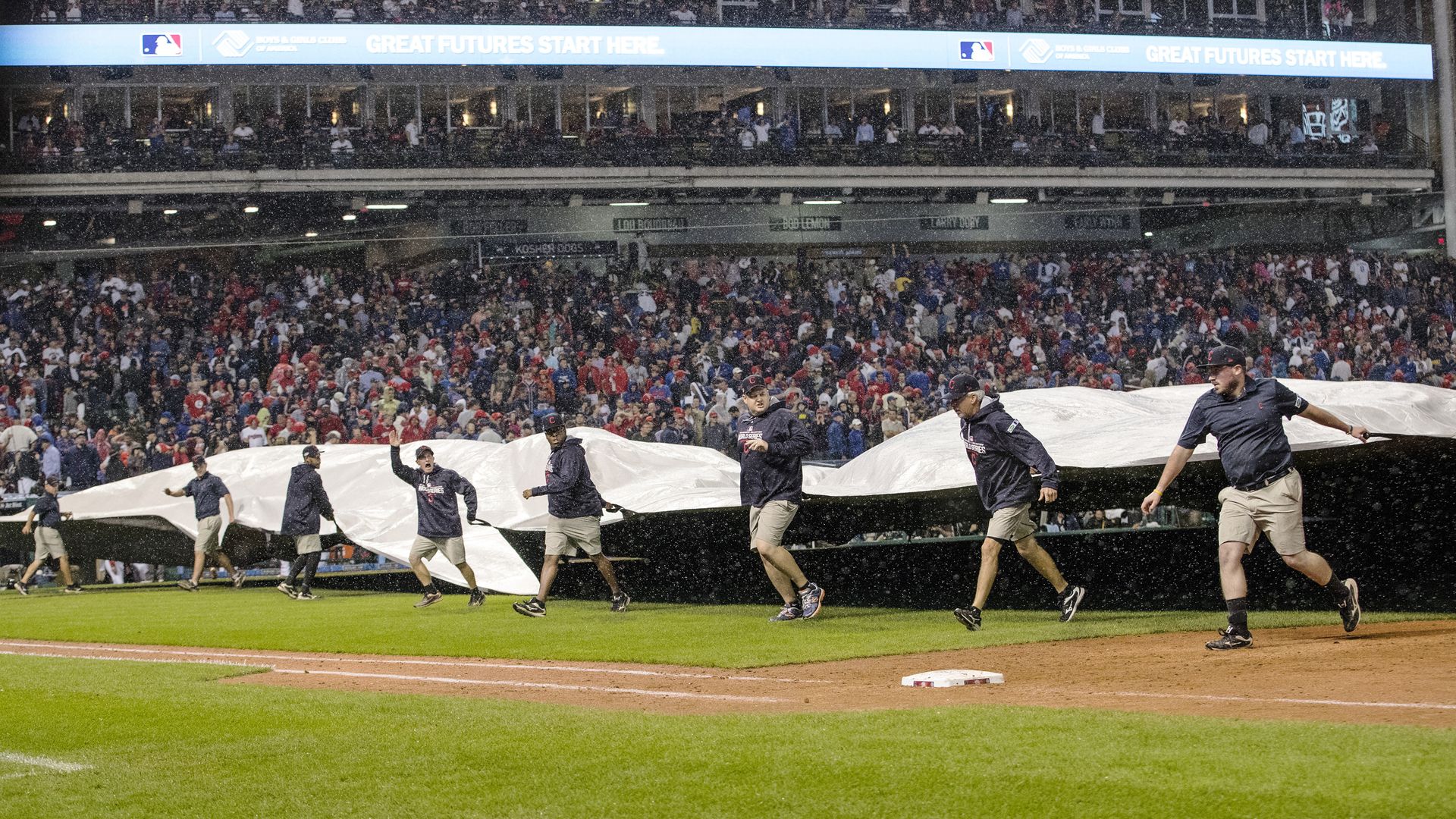 Grounds crew members pull out a tarp to cover Progressive Field in the 2016 World Series