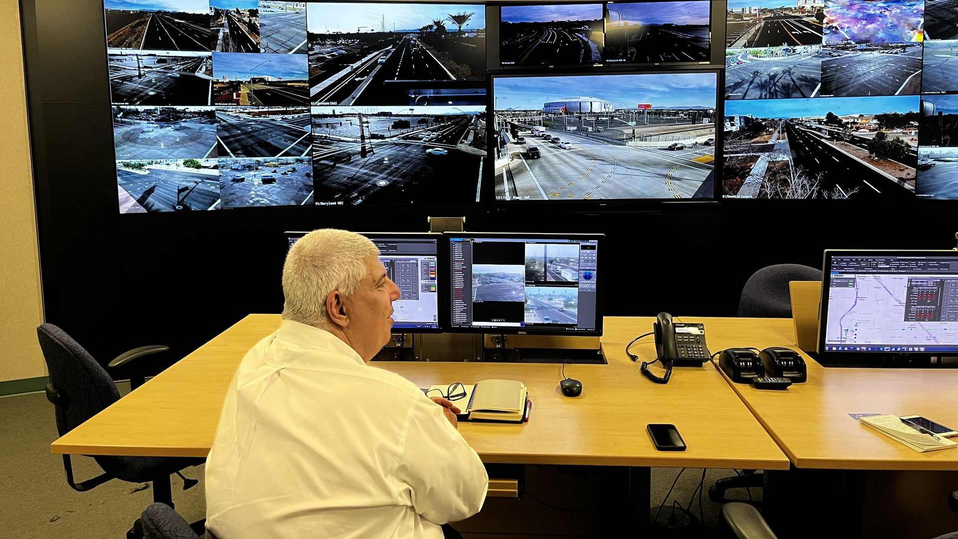 A man sitting in front of a wall of TV screens showing roadways. 