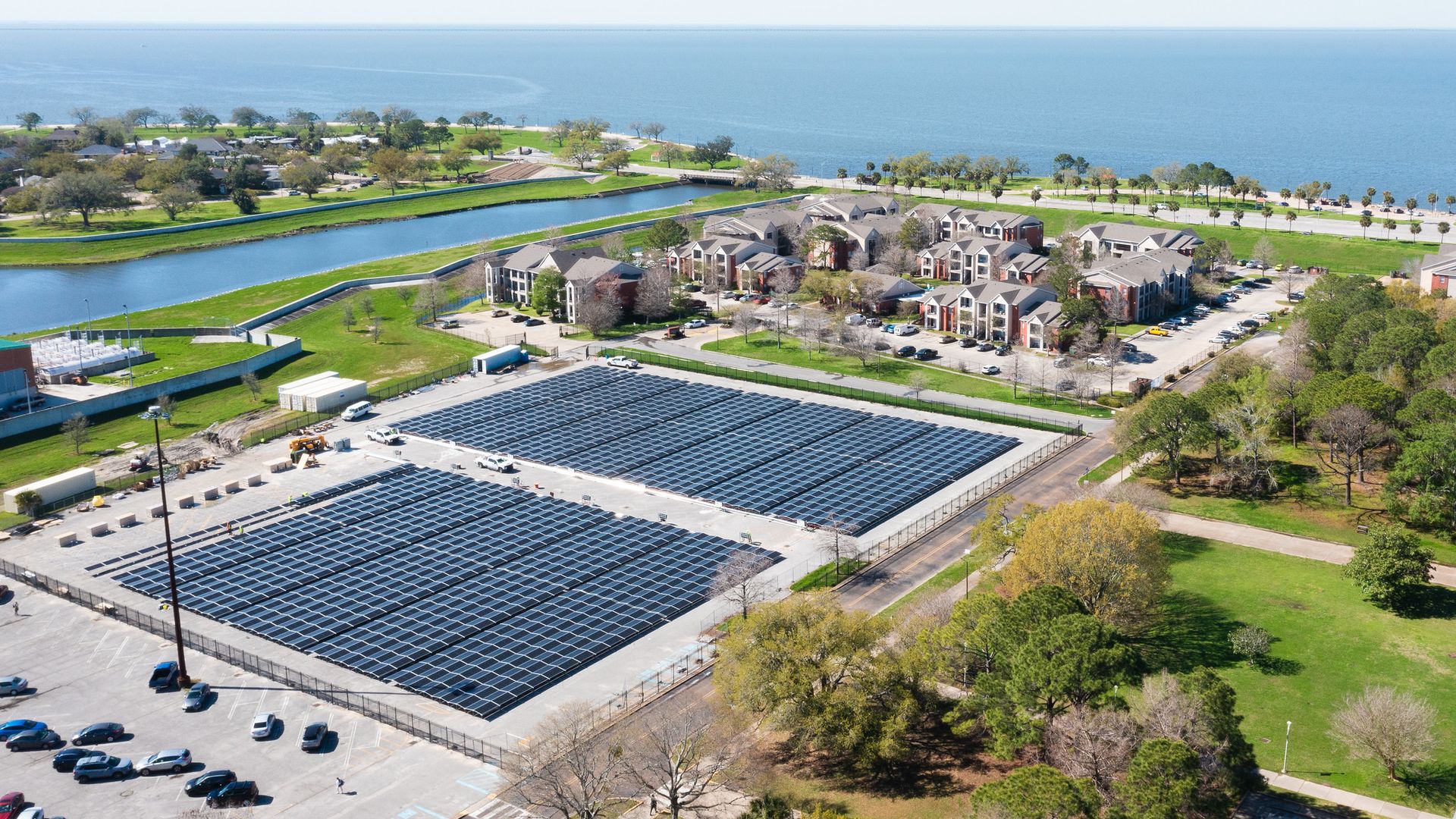Photo shows two large parking lots full of solar panels with the UNO buildings in the background with Lake Pontrchartrain.