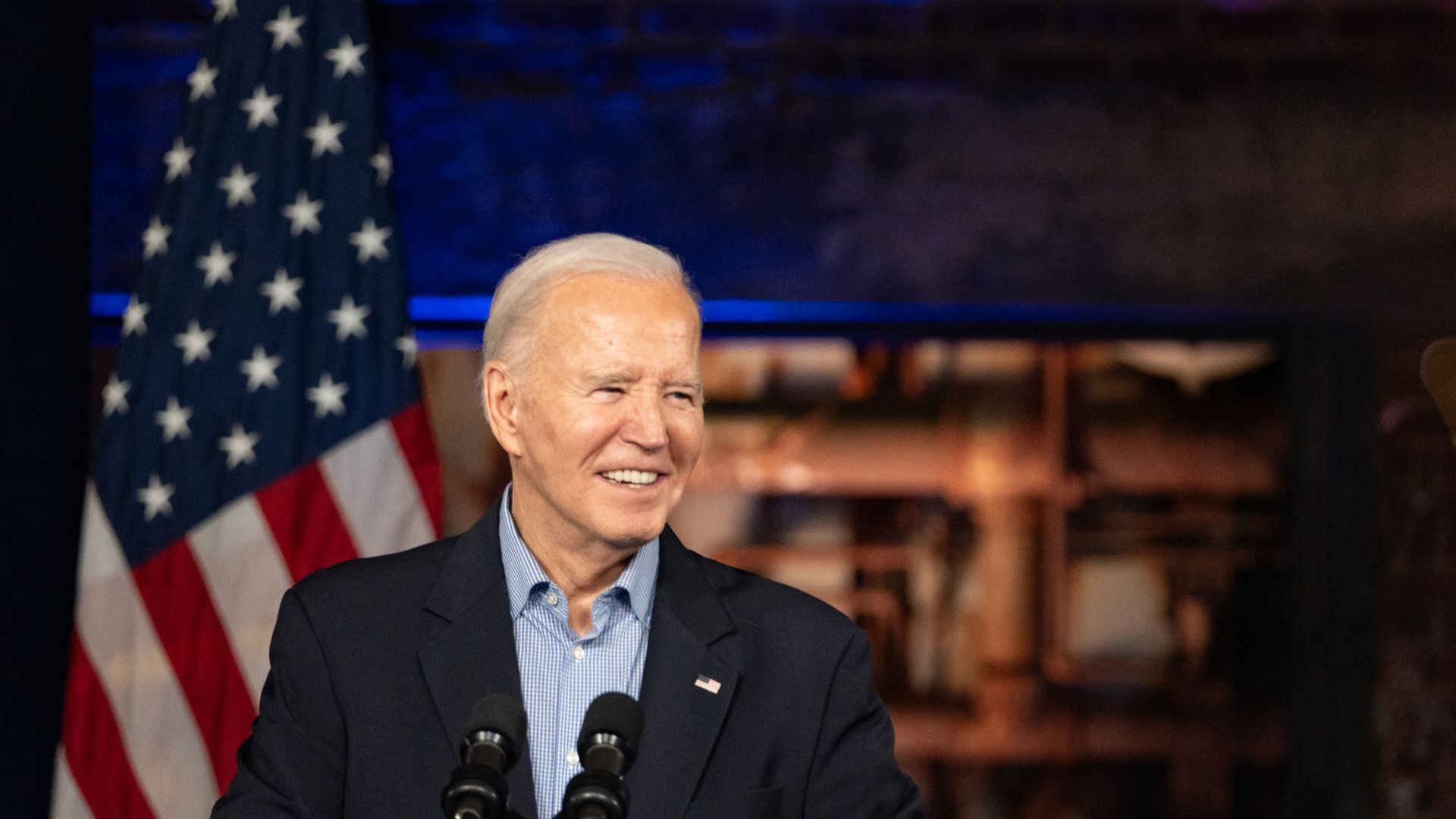Joe Biden smiles next to a flag