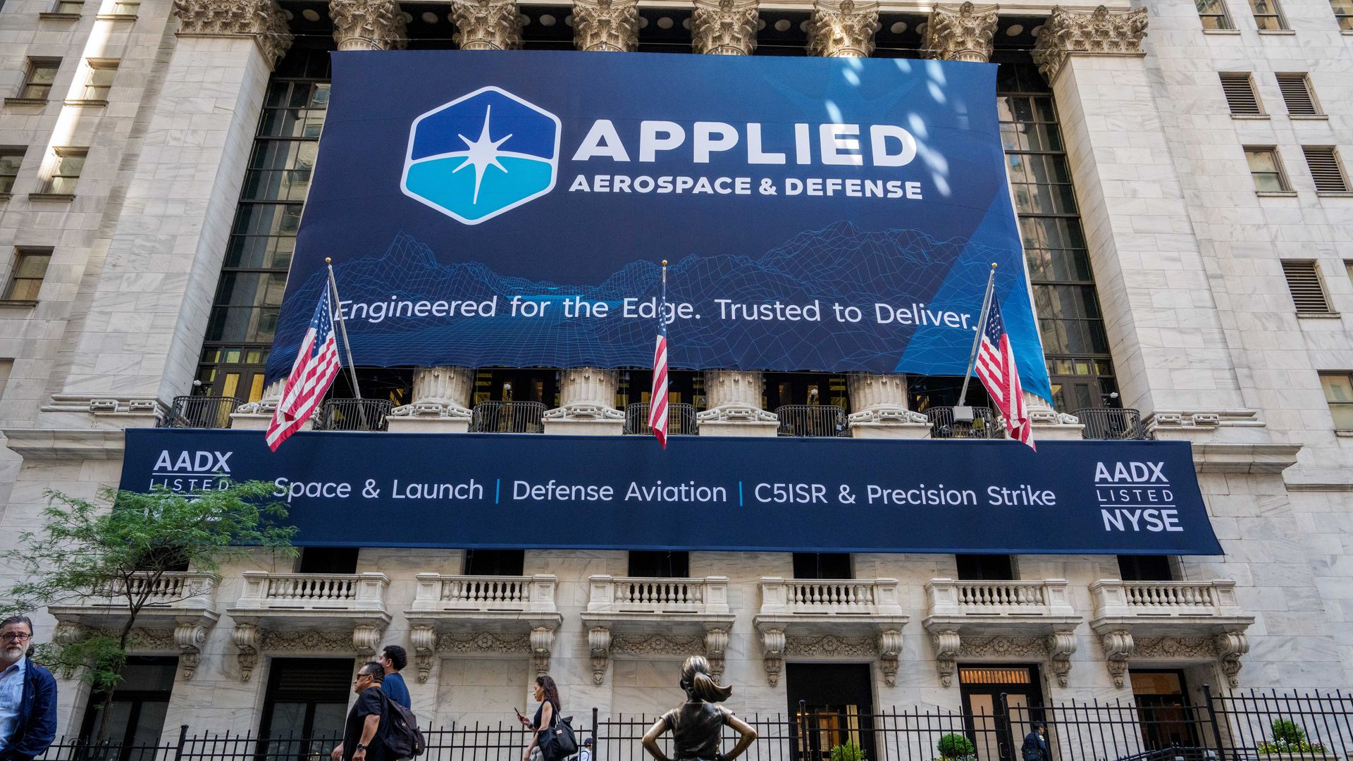 Front of a historic marble building with a large blue banner reading "APPLIED AEROSPACE & DEFENSE" and a hexagon logo; the slogan "Engineered for the Edge. Trusted to Deliver." is visible below.