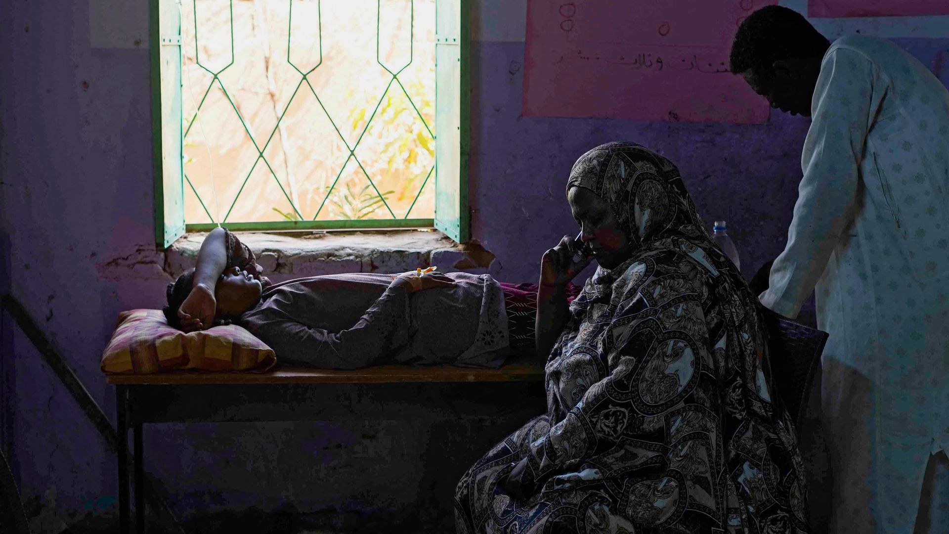 Relatives sit by a patient at a makeshift emergency room set-up by Sudanese volunteers in a school building in Omdurman