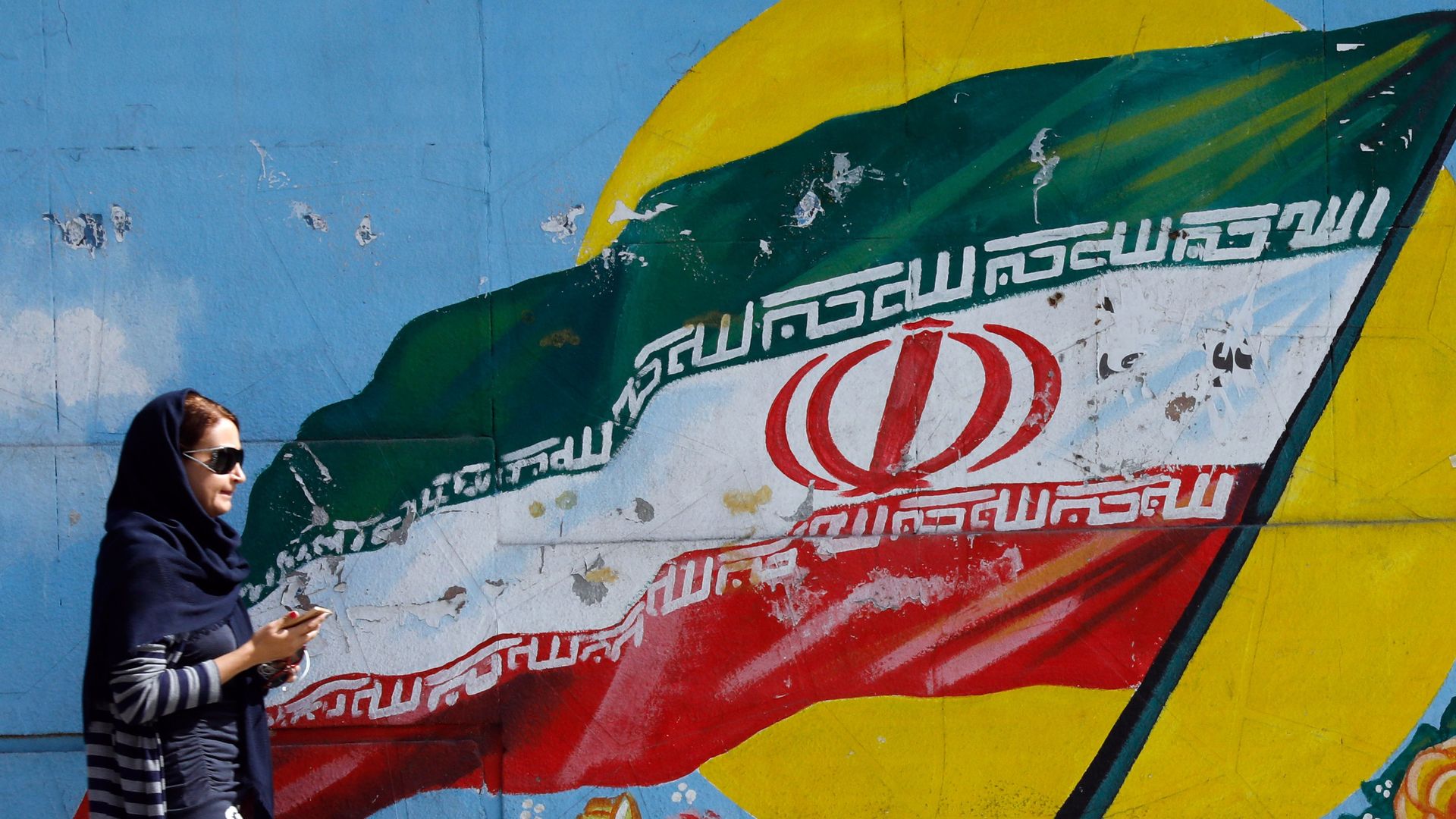 A woman walks by a mural of an Iranian flag
