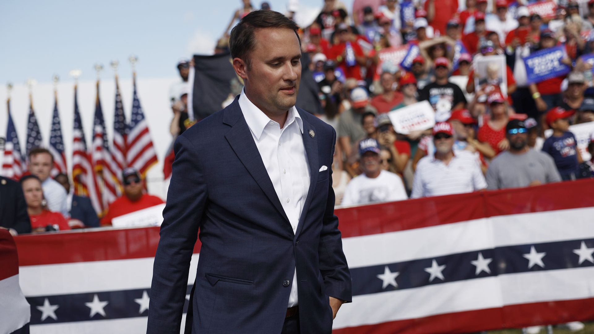 Jason Miyares in a suit walking in front of a crowd with American flags