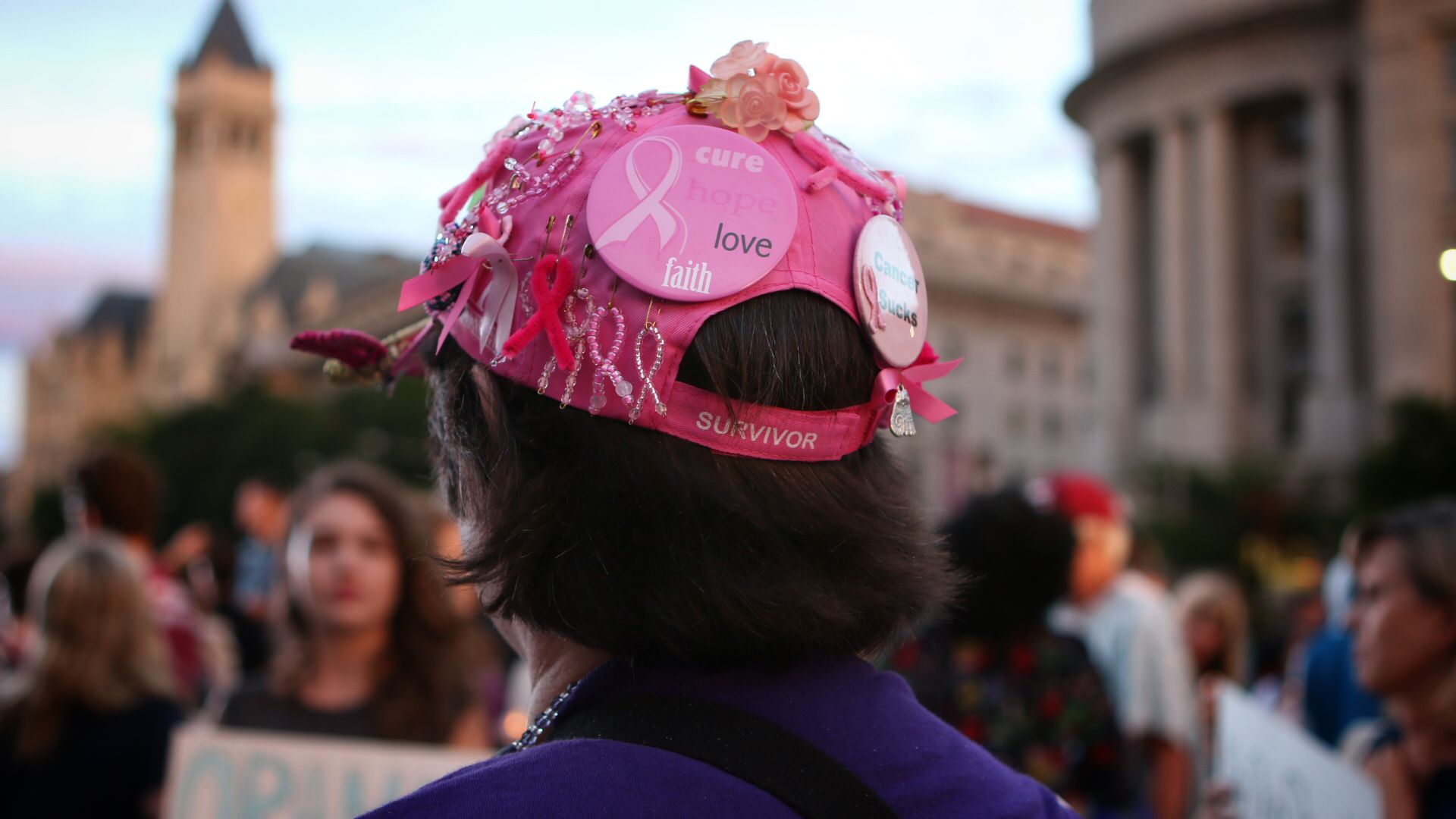 Photo of the back of Helen Webb, who is wearing a pink cap that says "survivor" and has pink breast cancer ribbons attached