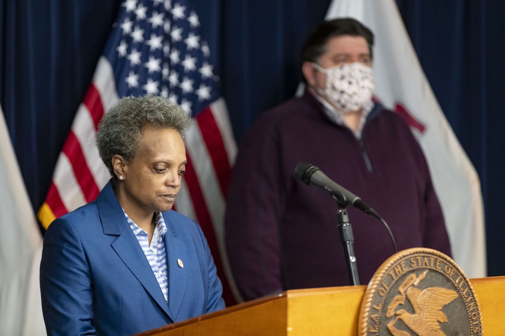 Mayor Lori Lightfoot behind a dais with Gov. JB Pritzker in the background wearing a mask.