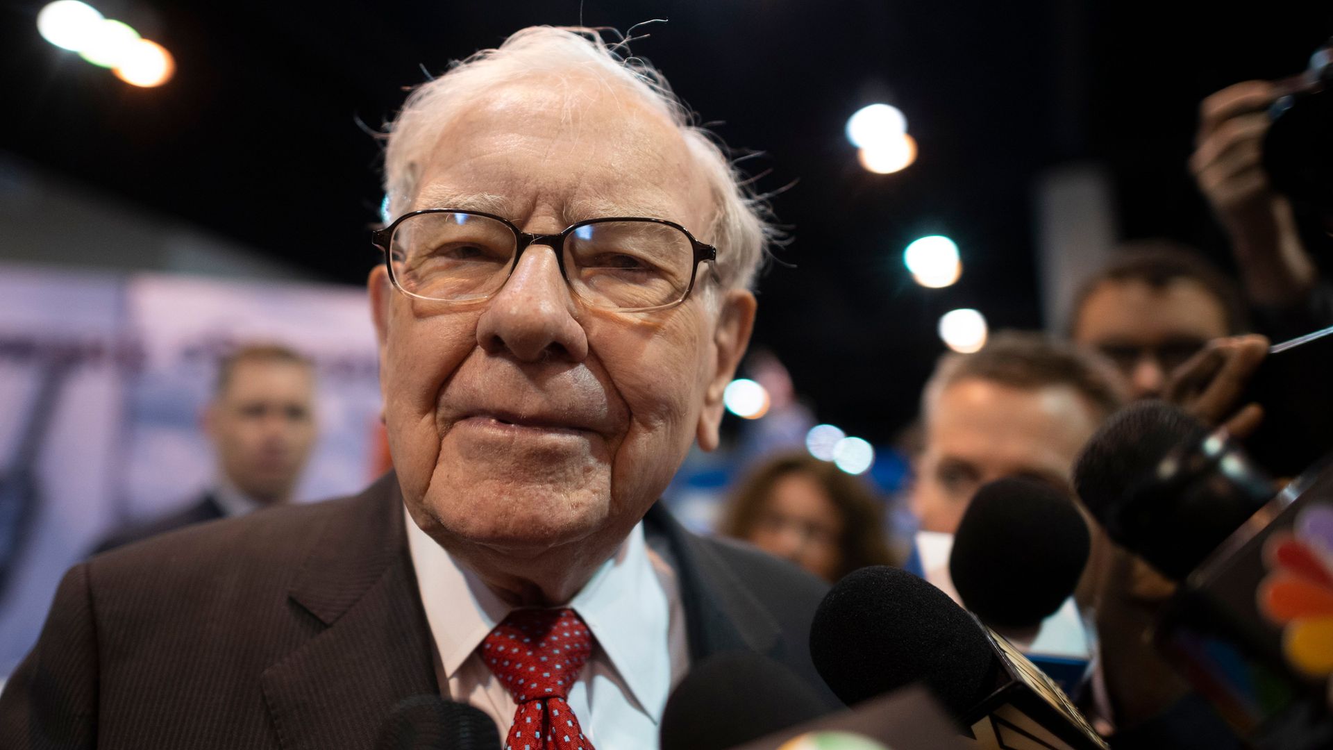 In this image, Warren Buffett stands in front of microphones