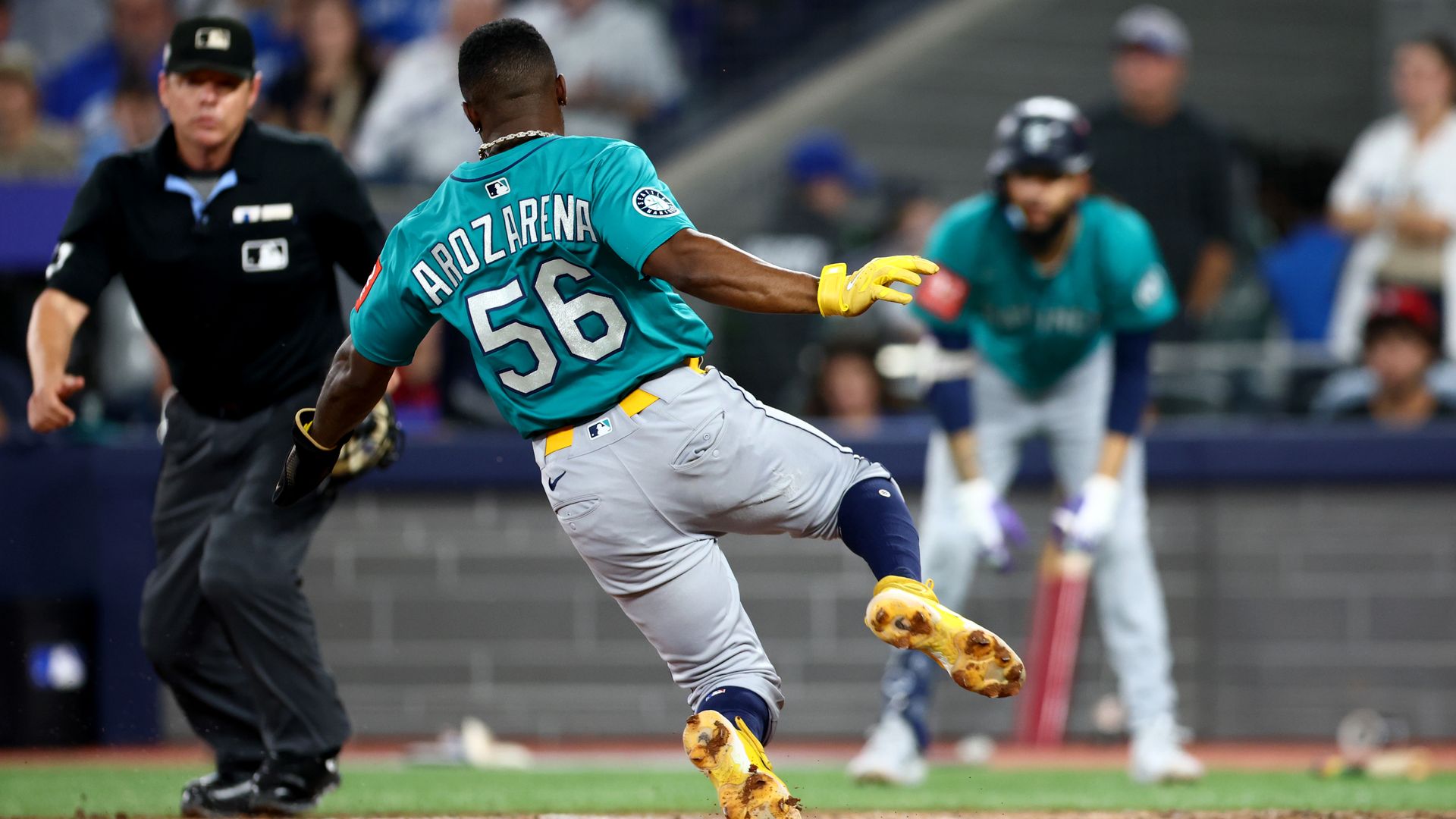 A baseball player wearing a teal jersey with the number 56 slides toward a base as the umpire watches closely.