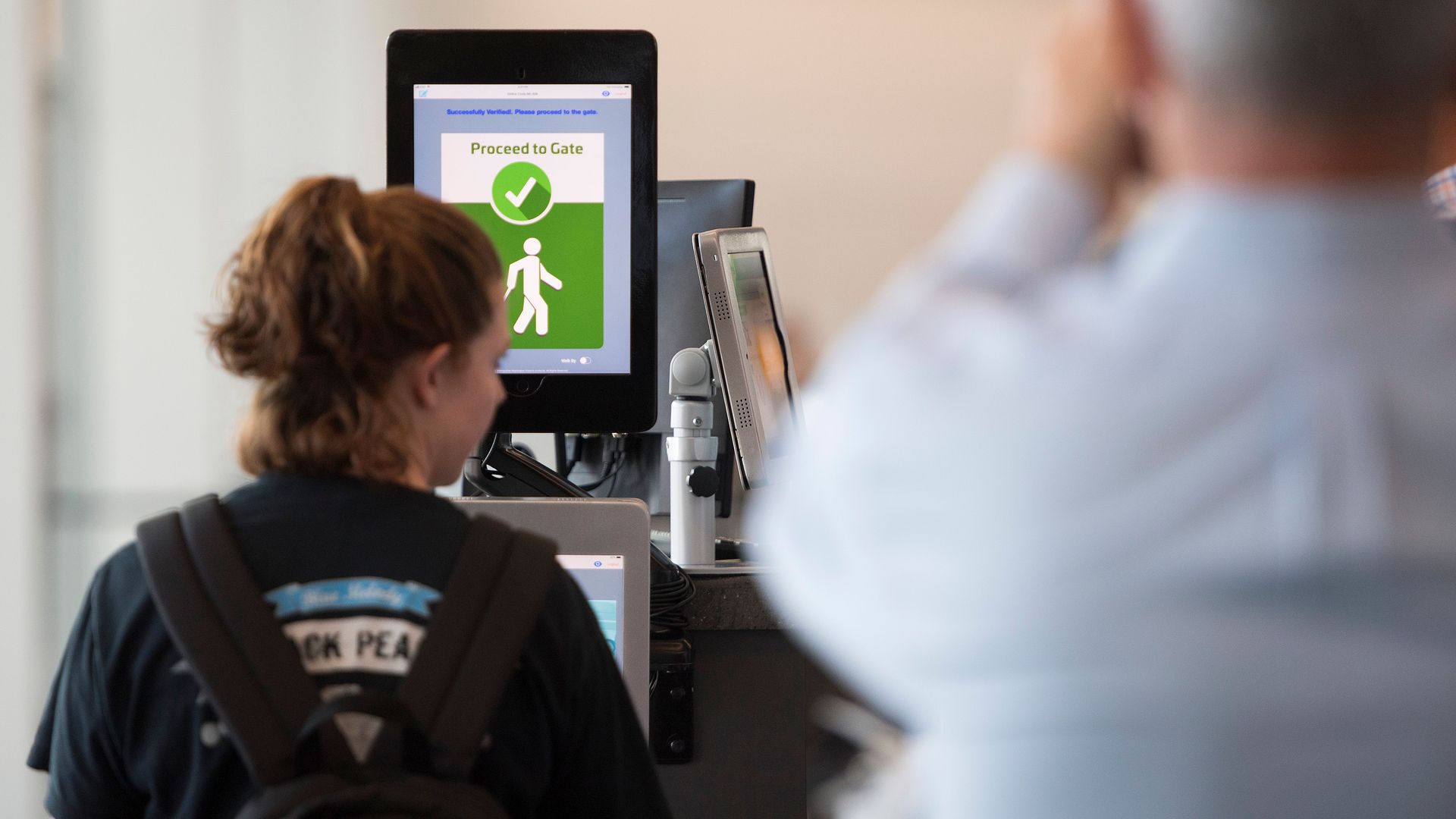Photo of a woman in front of a screen with a checkmark and the words "Proceed to gate."