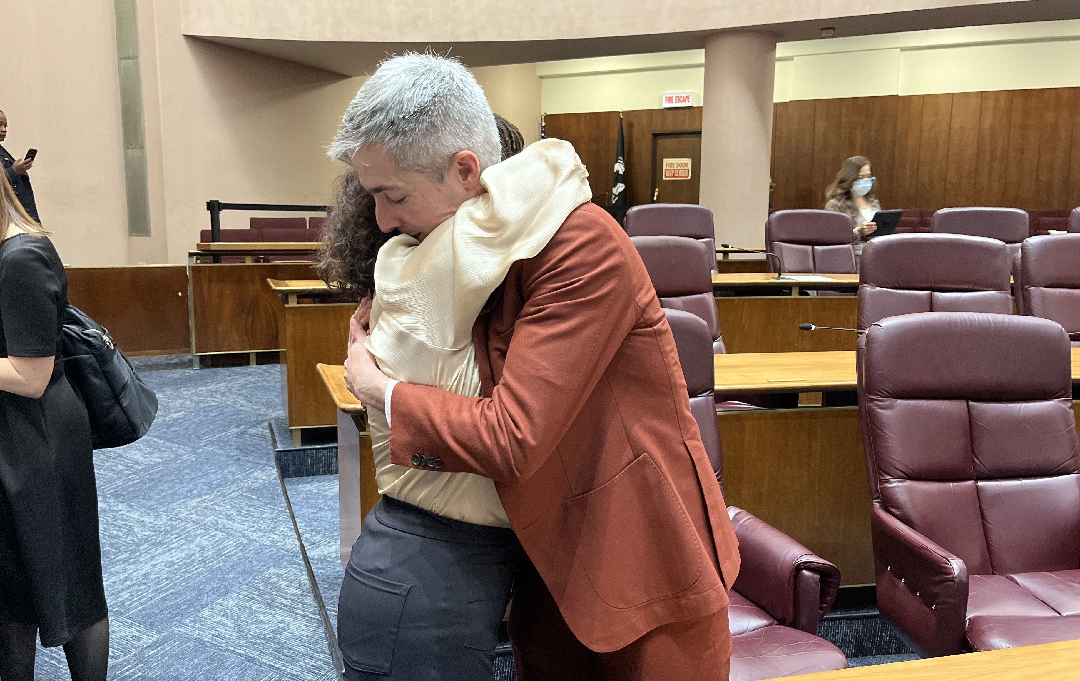 Two alders hug in City Council.