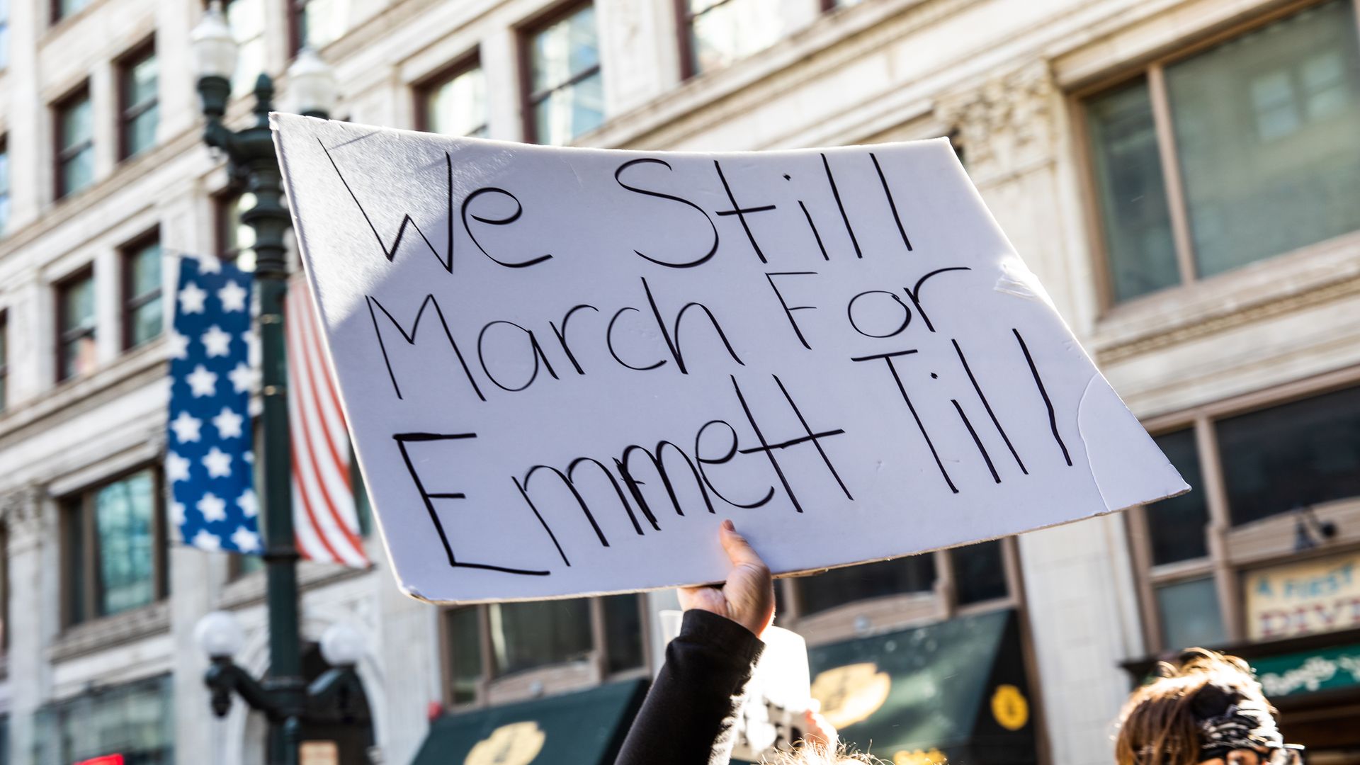 Photo of a protester holding a sign that says "We still march for Emmett Till" at a rally outdoors