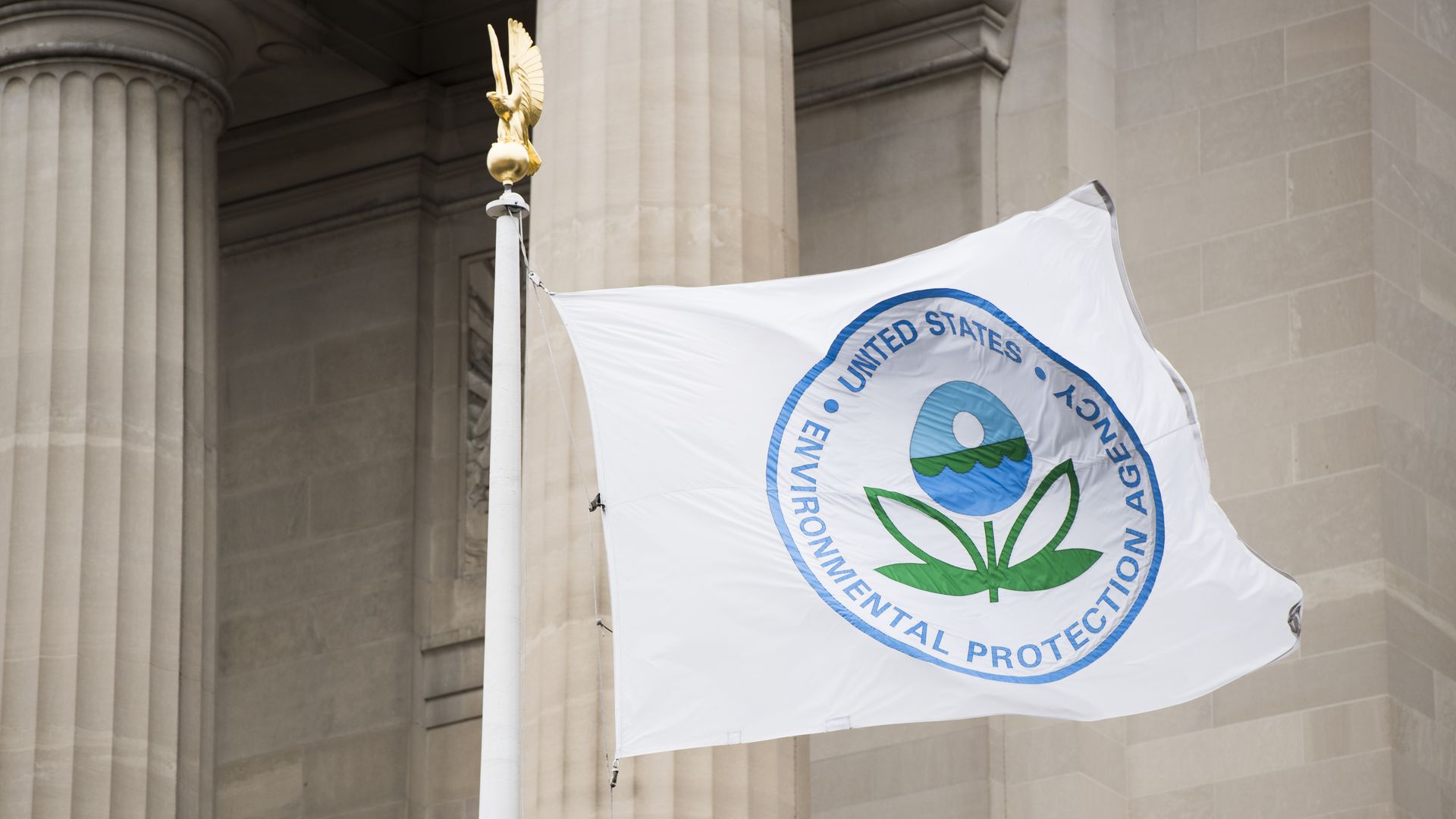In this image, the EPA logo is displayed on a flag in front of a pillared federal building.