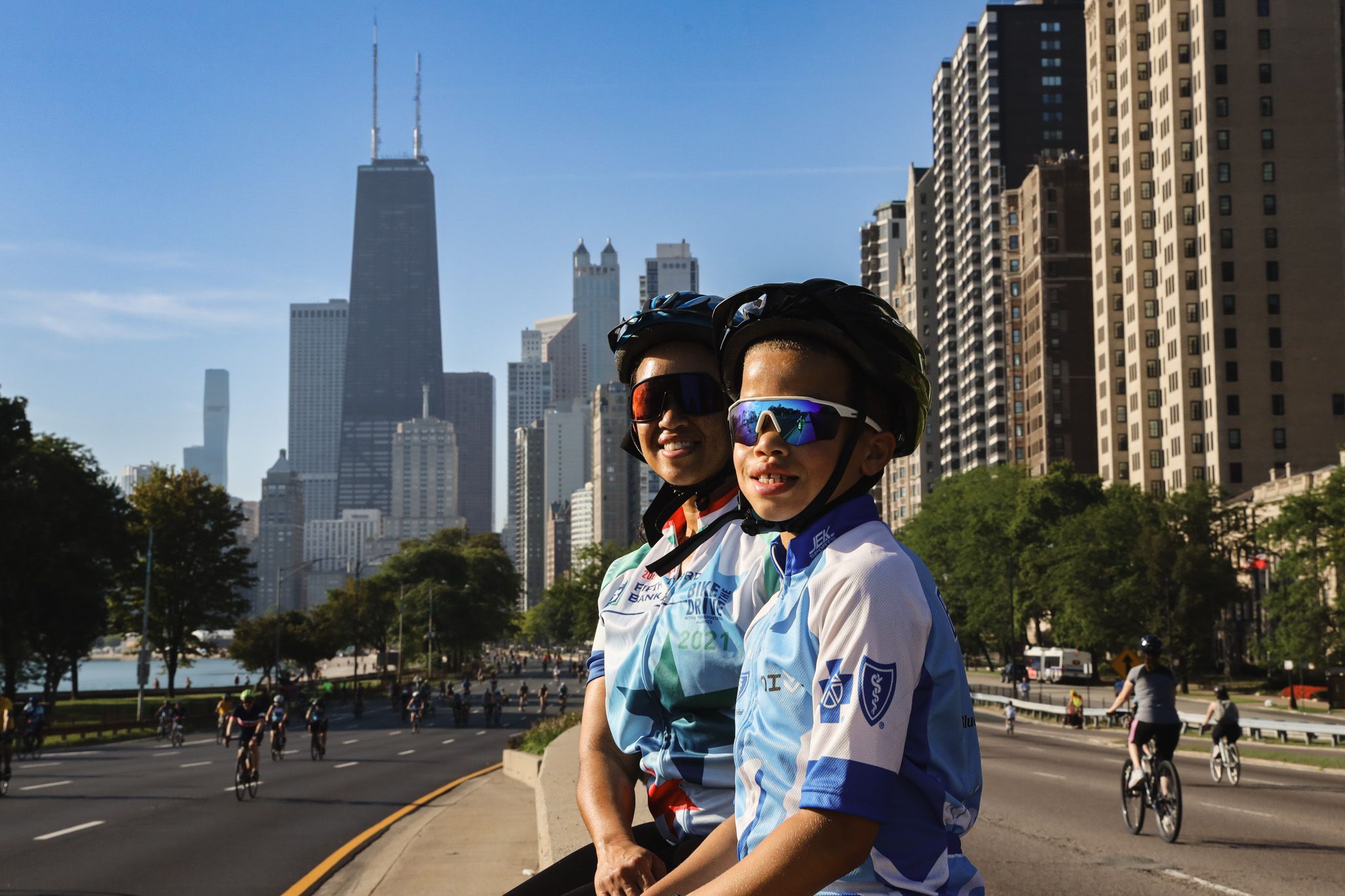 A mother and child wearing helmets and glasses pose with the Chicago skyline in the background