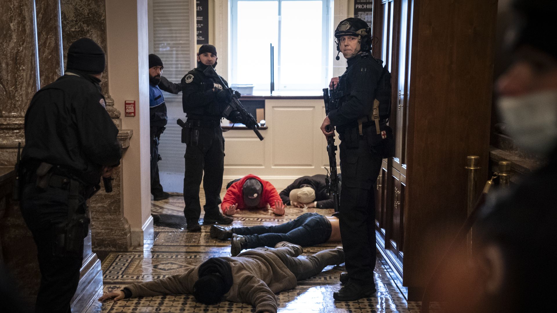 Photo of armed USCP officers standing in uniform while watching over rioters face down on the ground