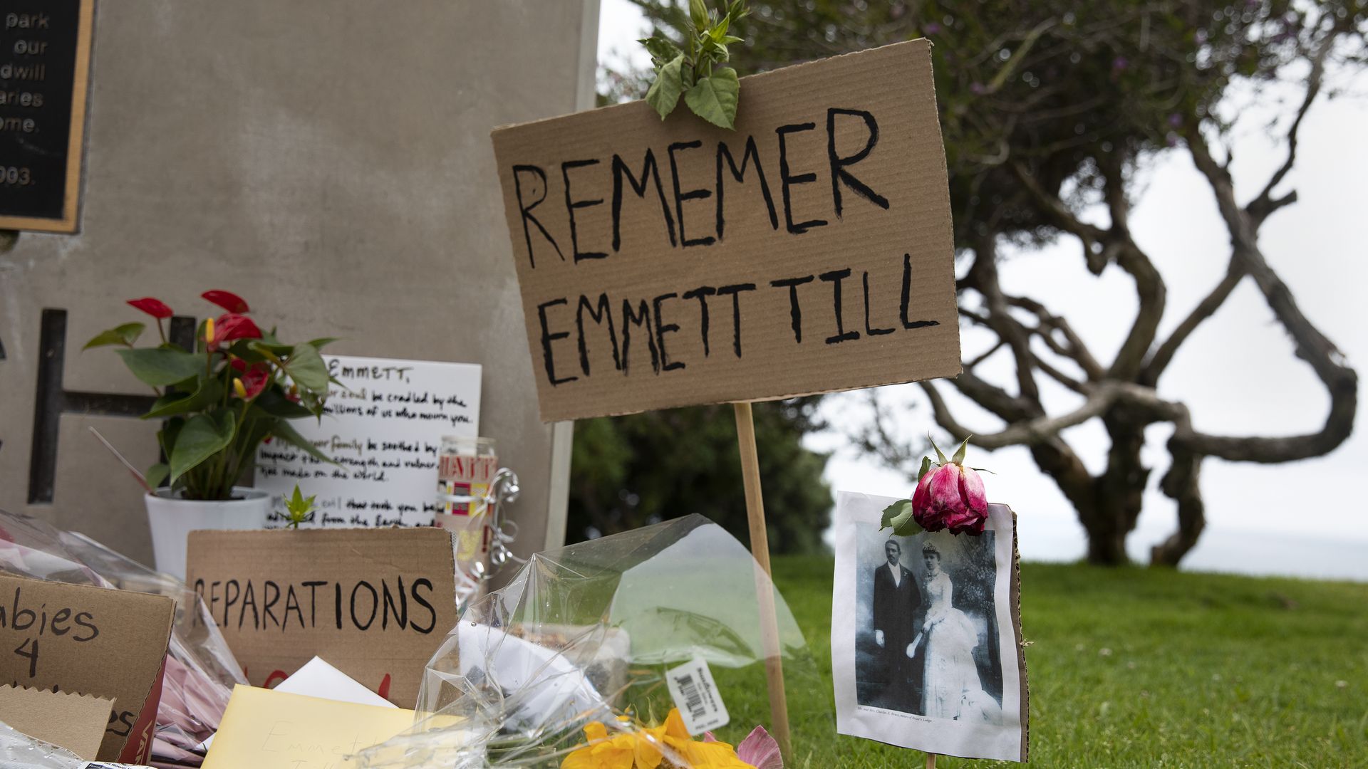 Photo of a memorial that shows flowers, photos and signs, one of which says "Remember Emmett Till"