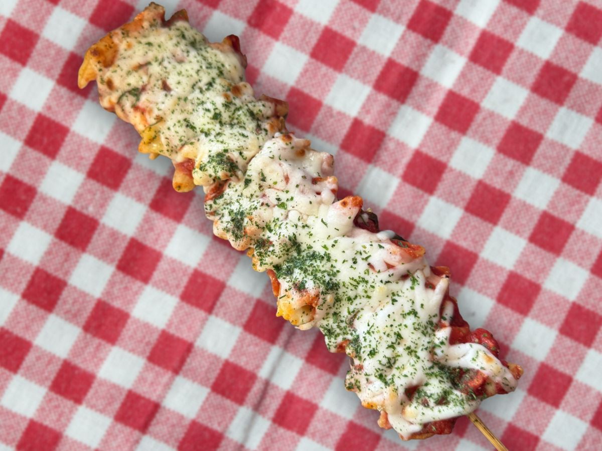 A line of pasta topped with melted cheese and a green herb on top of a red gingham table cloth.