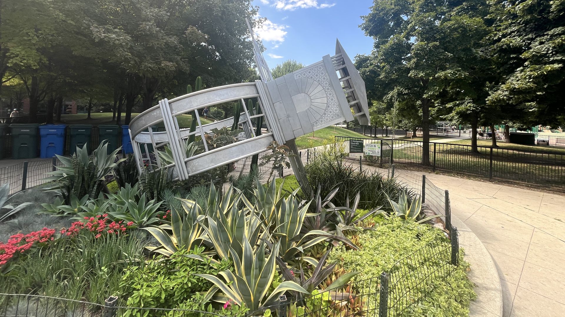 Stainless steel sculpture on its side in the middle of a garden.