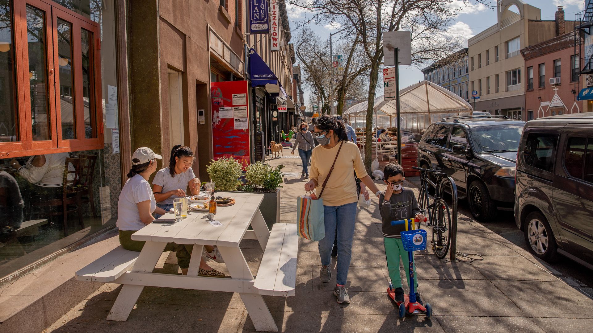 Pedestrians wearing protective masks walk past diners eating outdoors in Brooklyn.