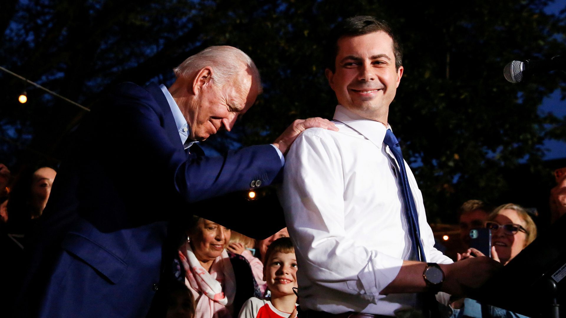 Joe Biden holds onto Pete Buttigeg's shoulders, as both men smile in front of a crowd.