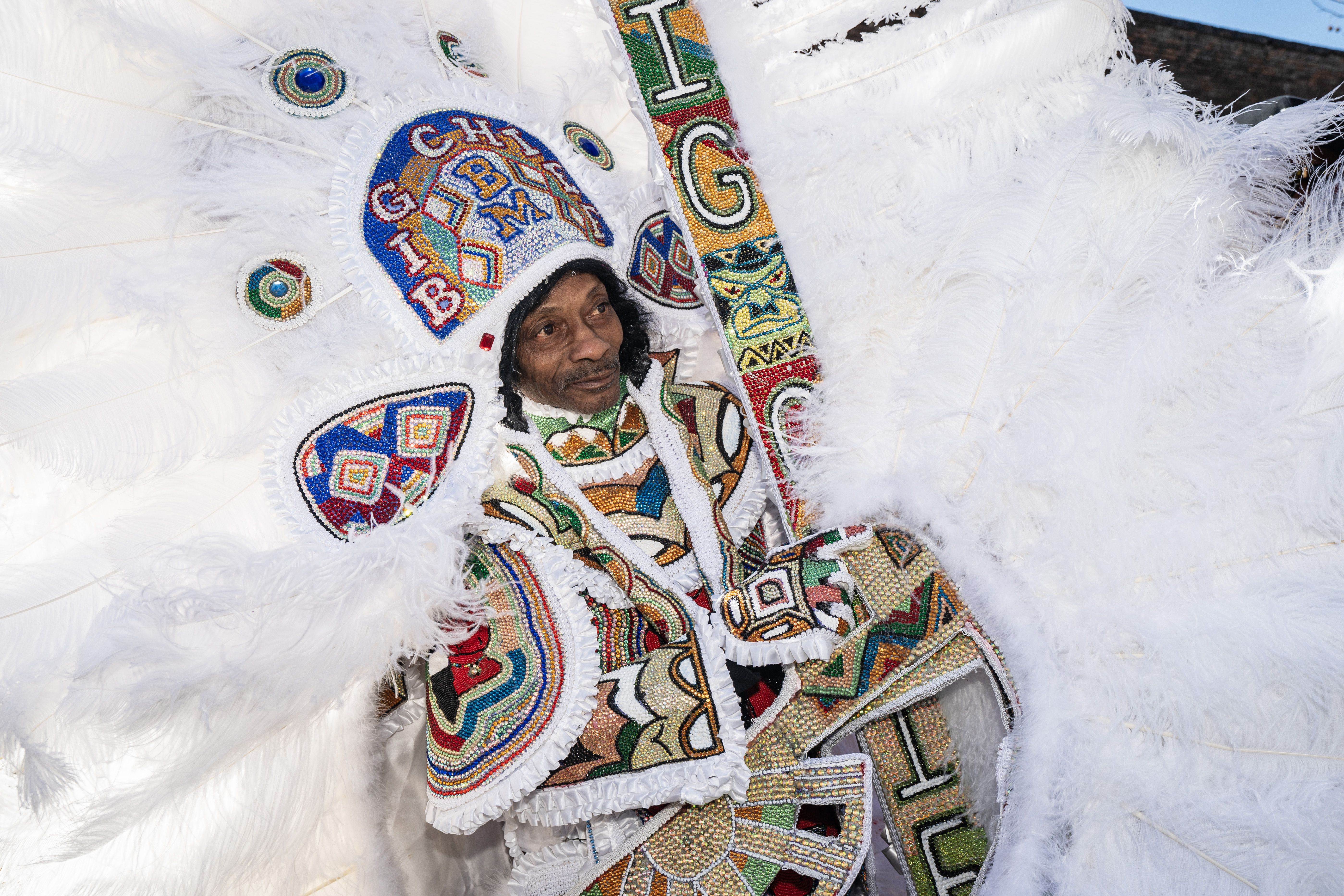 Photo shows a Mardi Gras Indian in a colorful feathered suit
