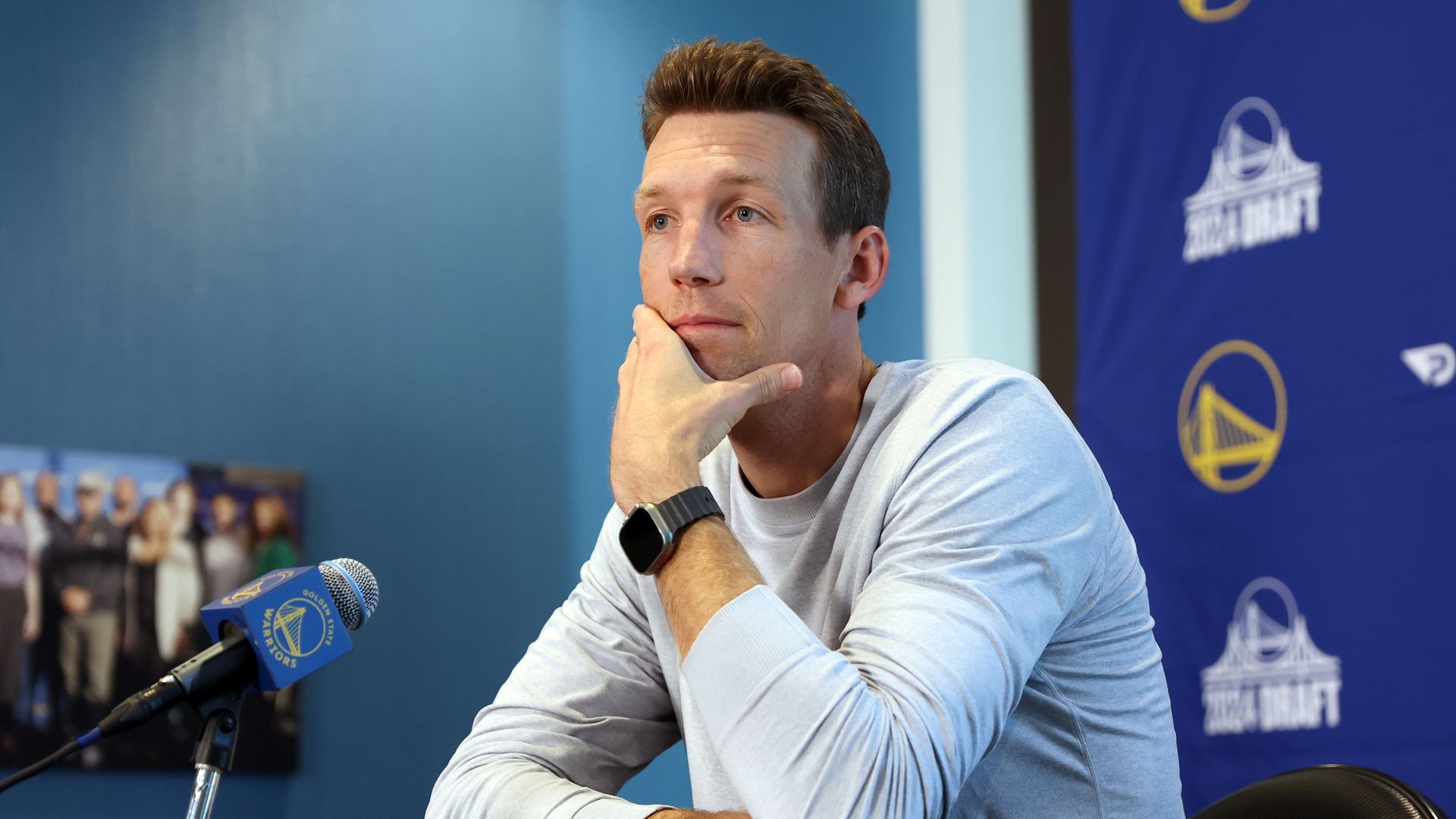 A man in a white shirt sits at a podium with a pondering look on his face