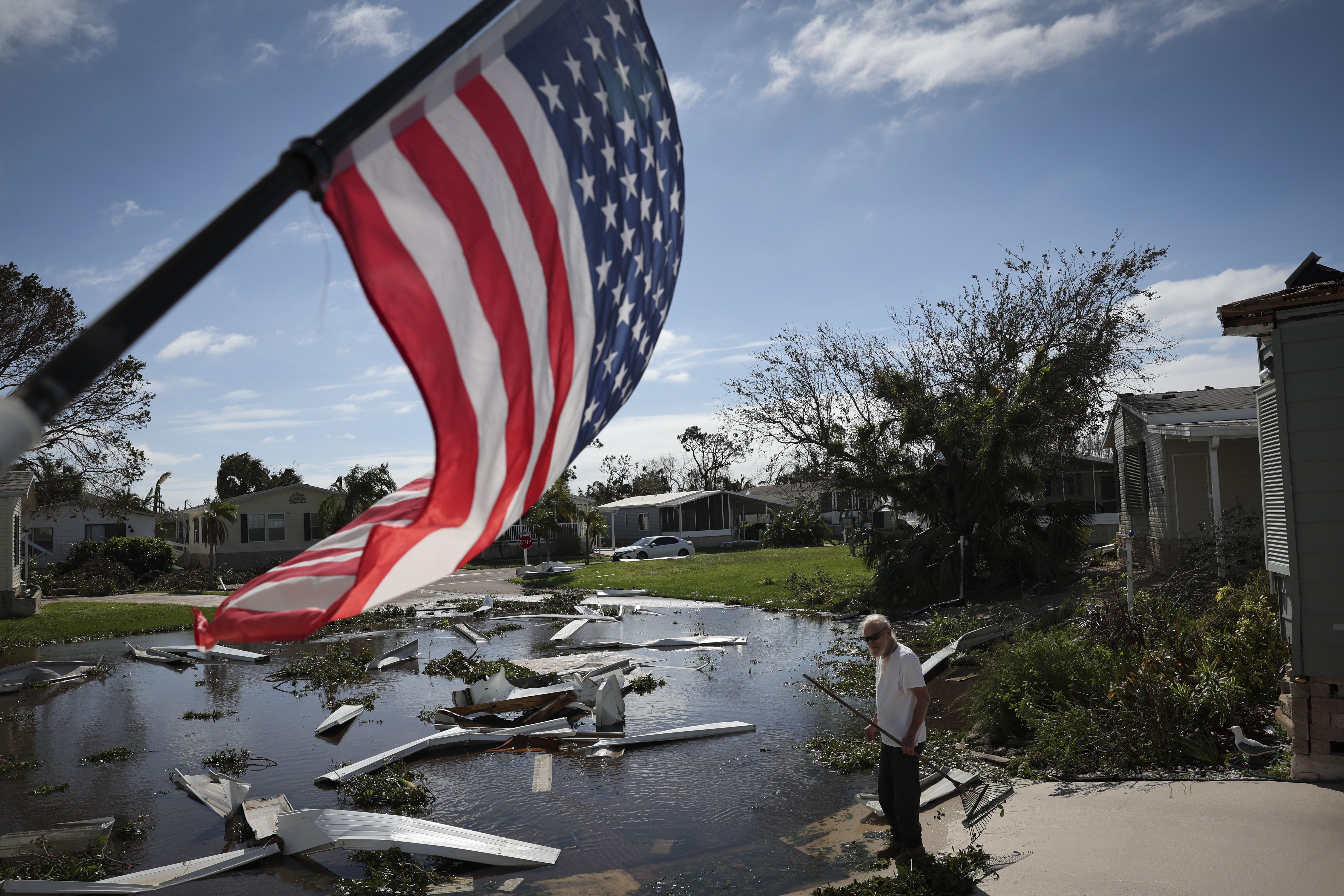 man cleans up debris after a hurricane next to an American flag