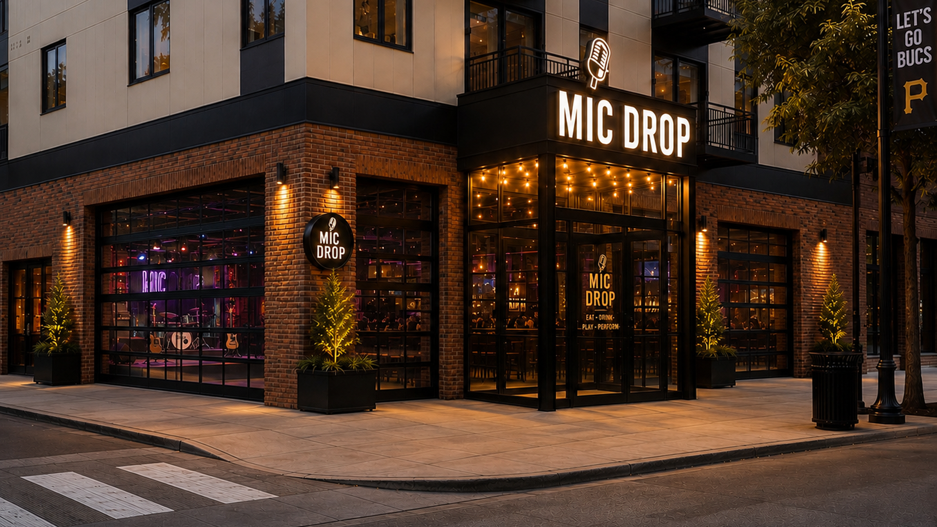 Evening street view of a brick-and-glass building with a restaurant named "MIC DROP"; a bright microphone sign above glass doors, warm interior lights, large windows, and potted evergreens outside.