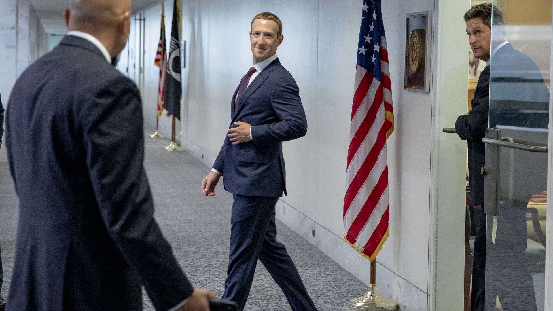 Photo of Facebook CEO Mark Zuckerberg exiting a security gate next to an American flag