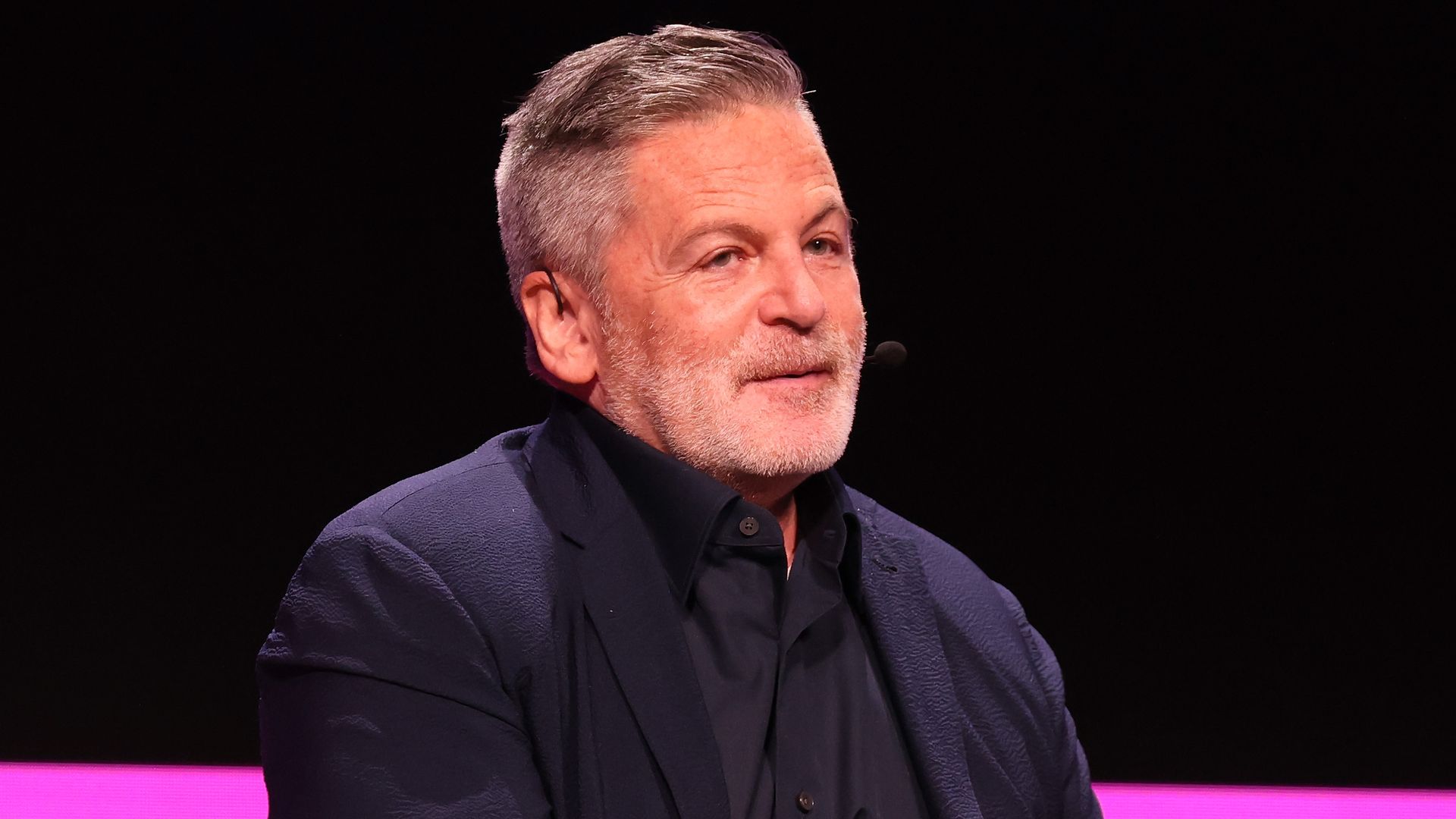 A man in a black suit and gray goatee