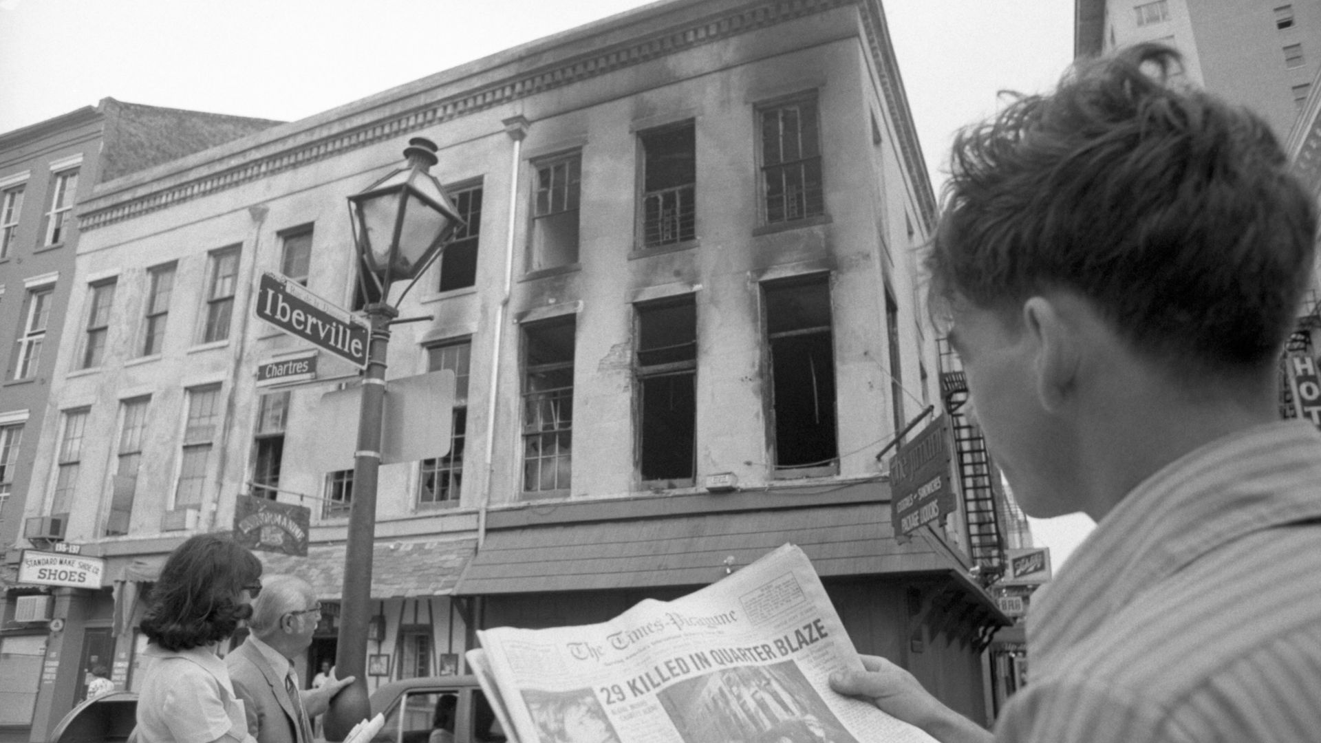 Image shows people reading a newspaper and looking at a burned building.