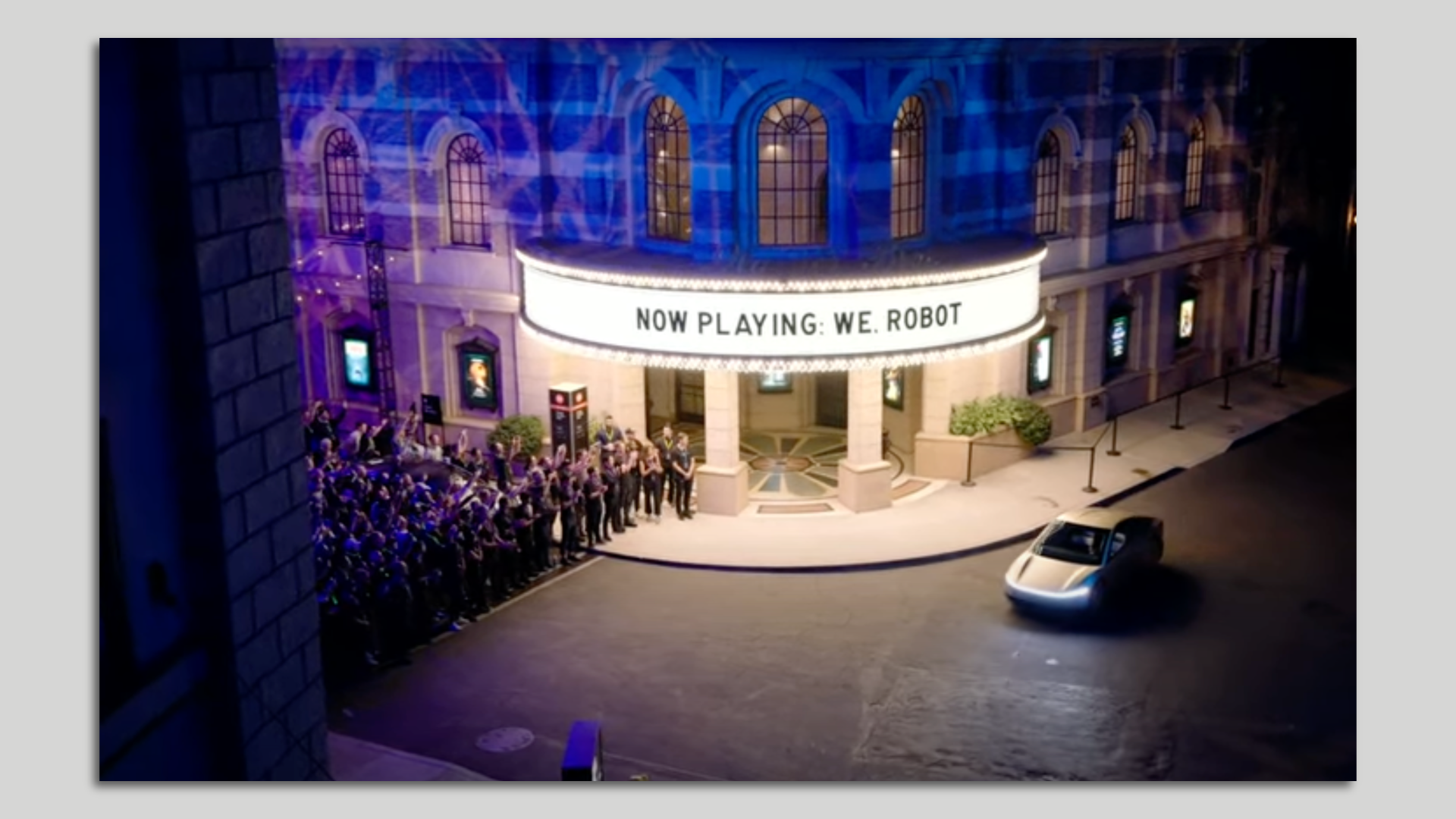 A Tesla robotaxi arrives in front of a theater with a sign above reading, "Now playing: We Robot"