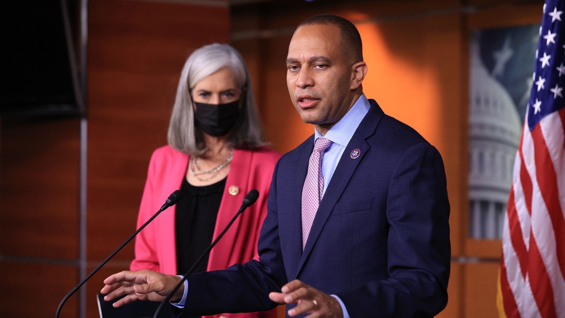 Reps. Katherine Clark, wearing a pink suit jacket over a black shirt, and Hakeem Jeffries, wearing a blue suit jacket, light blue shirt and pink tie, speak at a press conference.