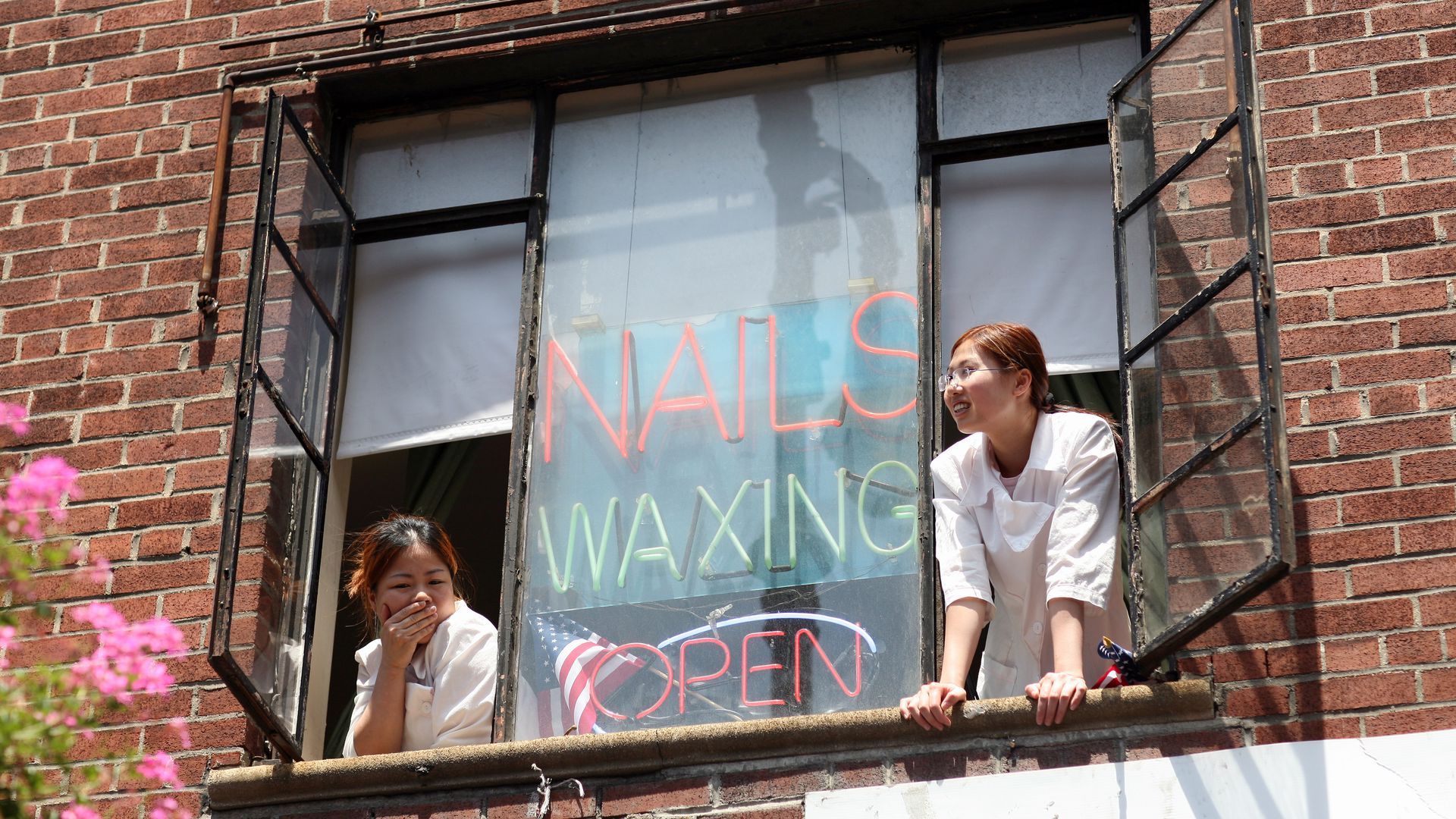 Two women look out the window of a nail salon