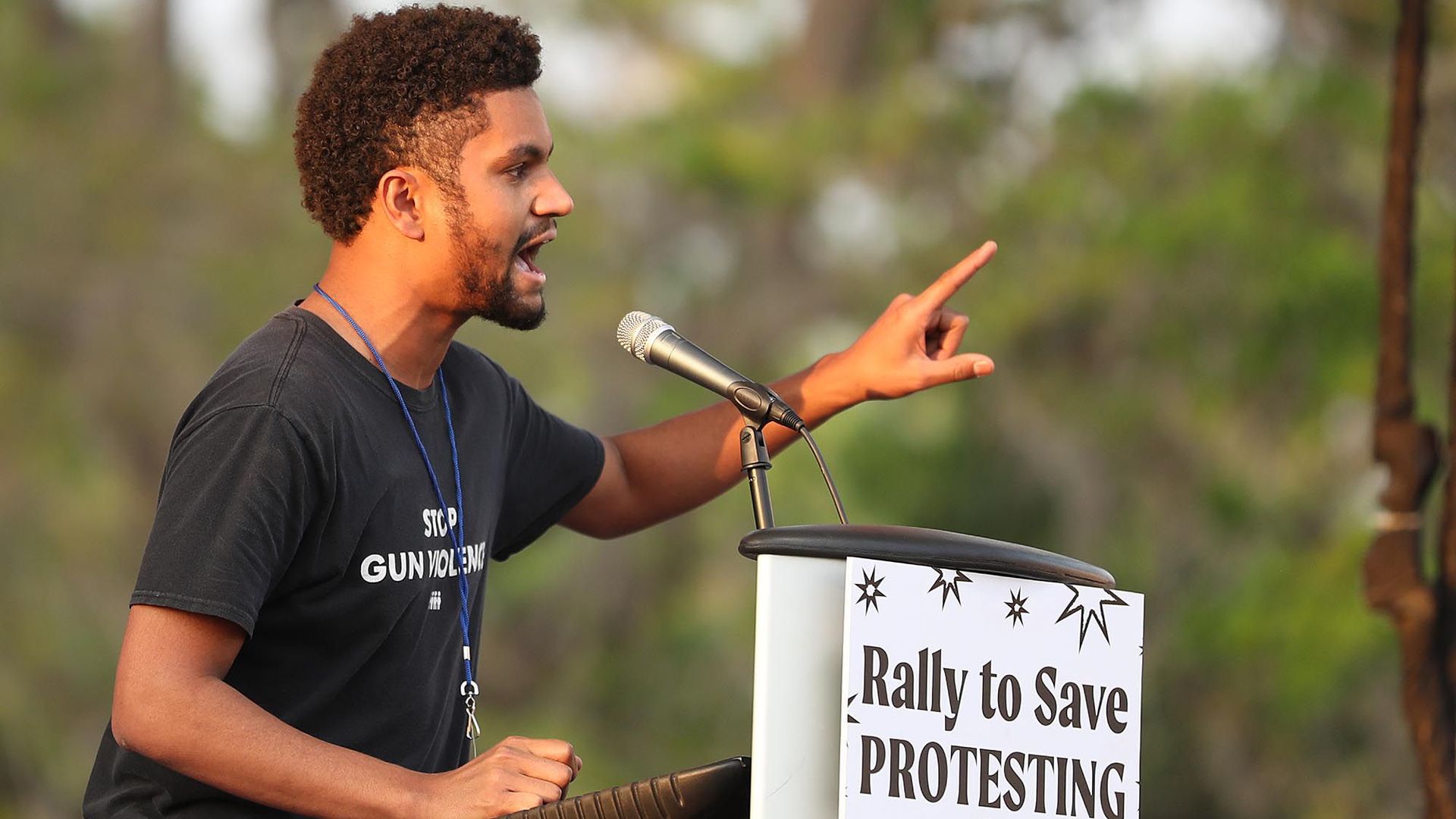 Maxwell Frost in 2021 speaks at a podium where a sign reads "Rally to Save Protesting."