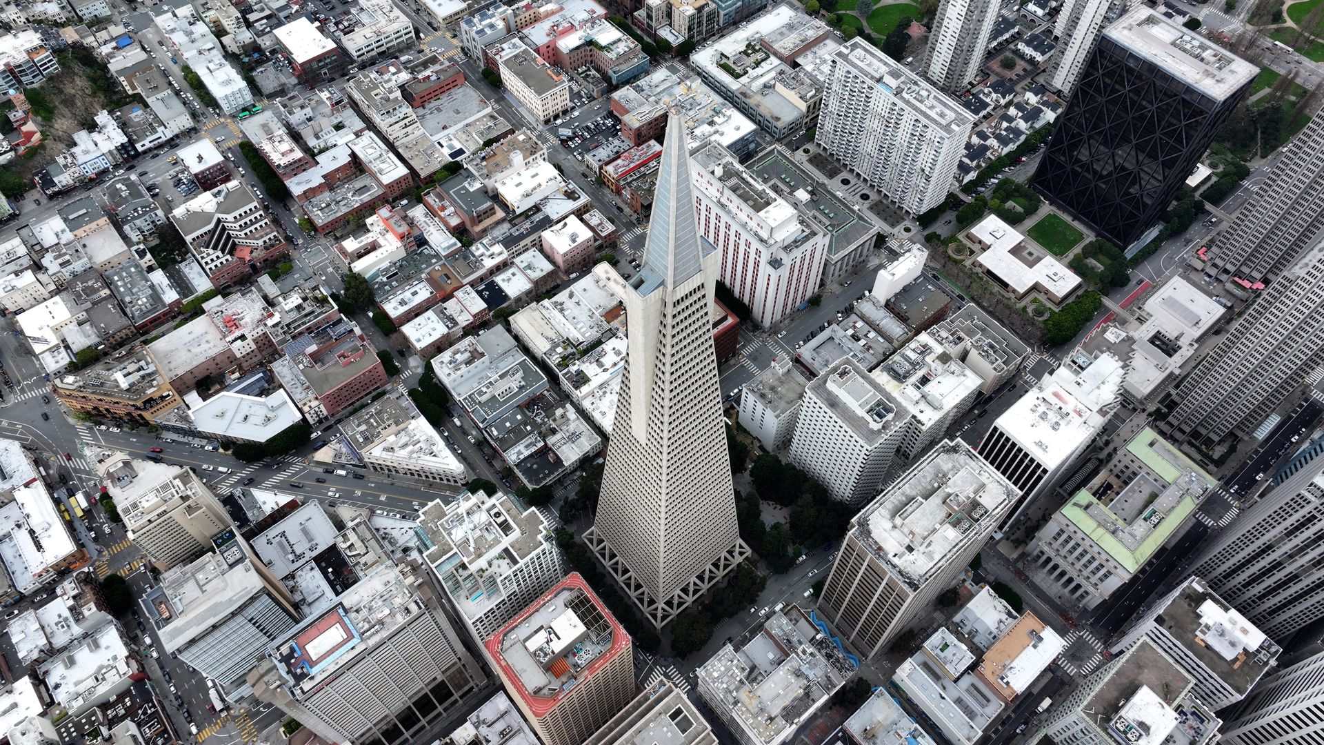 Aerial view of a dense city grid centered on the light-colored Transamerica Pyramid, surrounded by mid- and high-rise buildings and networked streets below.