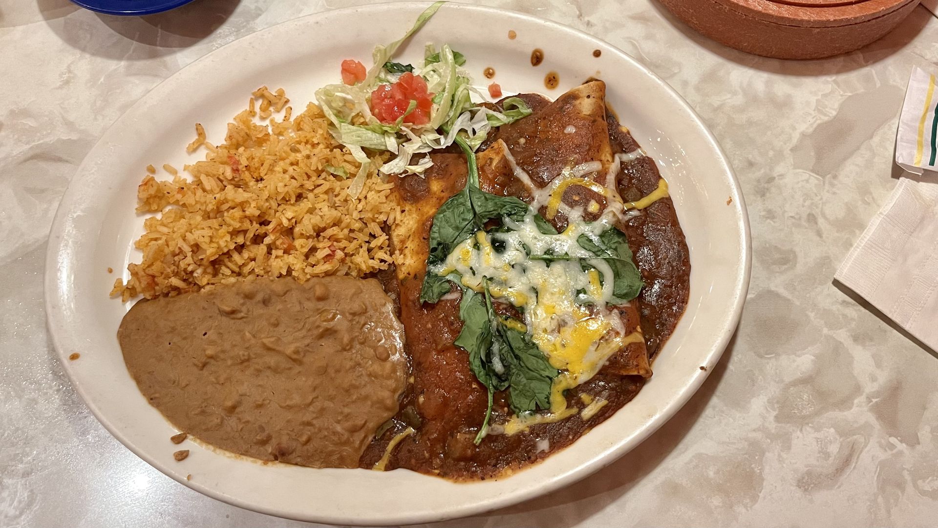 A plate on a table with rice, refried beans and enchiladas