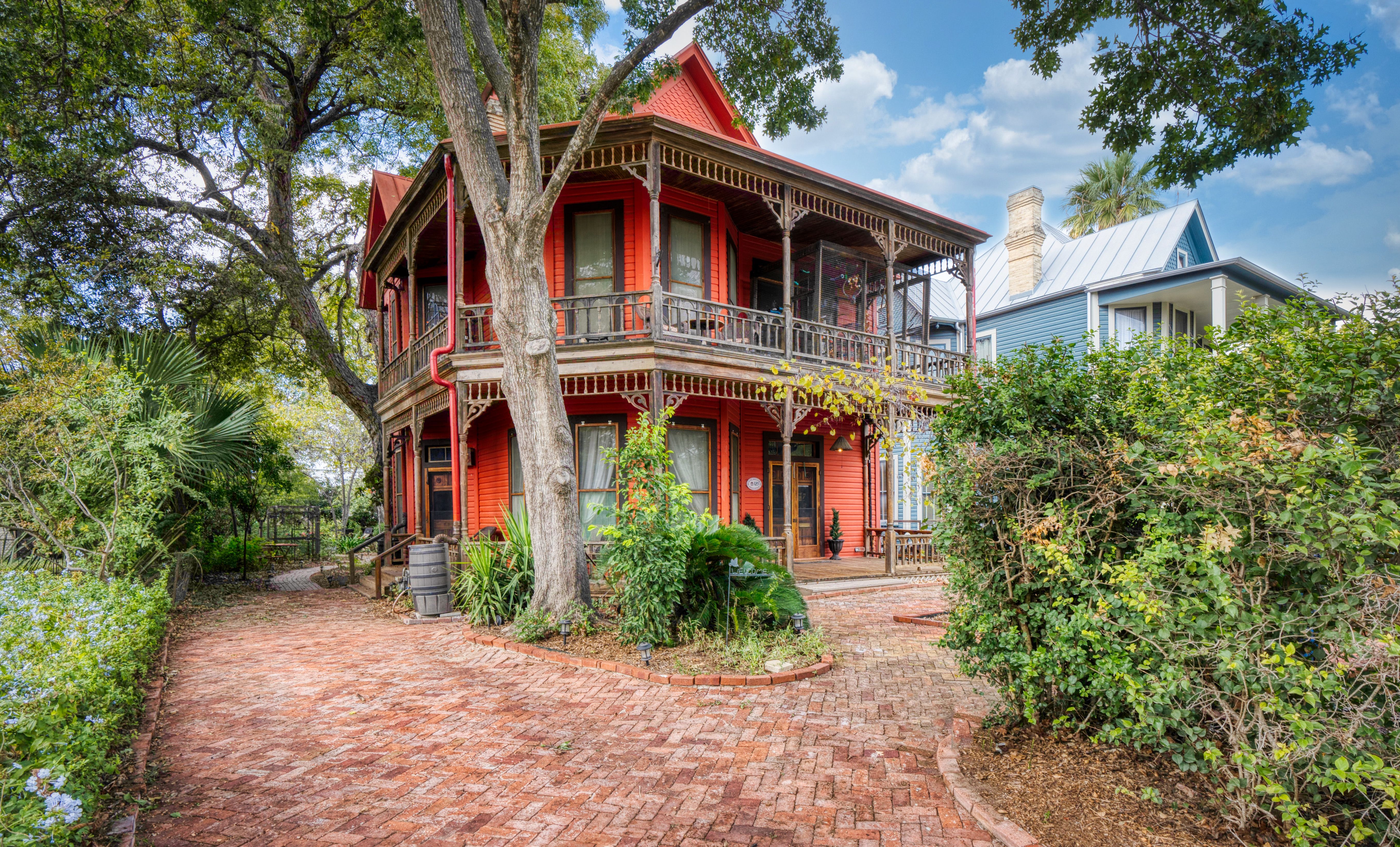 A bright red, historic looking home for sale in the King William neighborhood of Southtown, San Antonio. The home is surrounded by brick pavers and trees.
